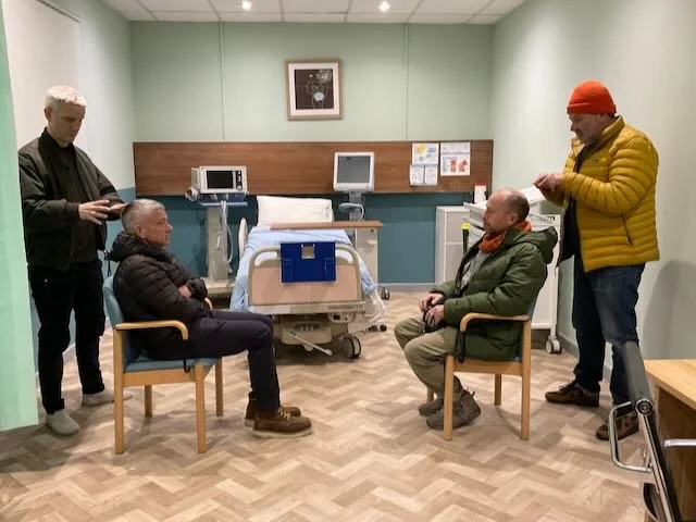   CONSULTATION ROOM 1 , our recommended HAIR TREATMENT PREP ROOM. That’s PATIENT 1 on our left, and PATIENT 2 sitting across from him. The room gives us so much—the correct floor for a medical prep room, the correct wall color, the correct ceiling. A