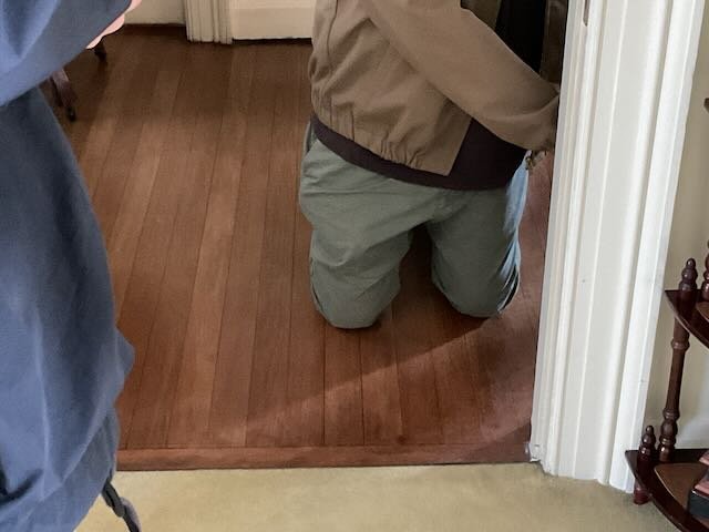  BACK TO…the LIVING ROOM, where TECH 1 is kneeling in a doorway, reaching back into another room. He holds up a… 