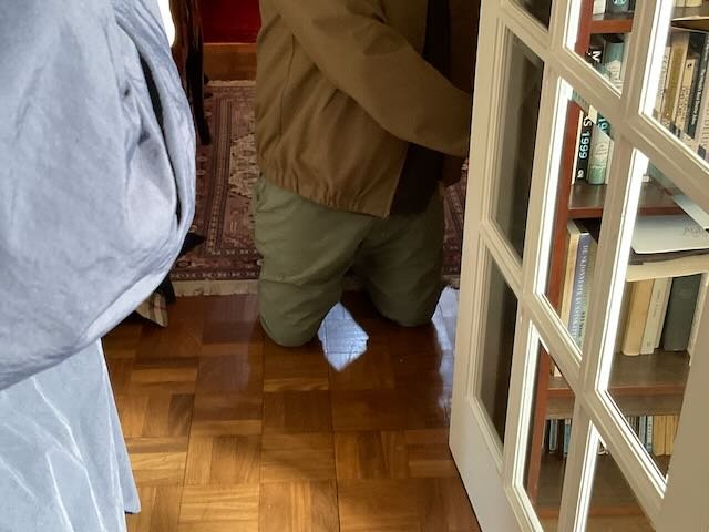  BACK TO…the LIVING ROOM, where TECH 1 is kneeling in a doorway, reaching back into another room. He holds up a… 