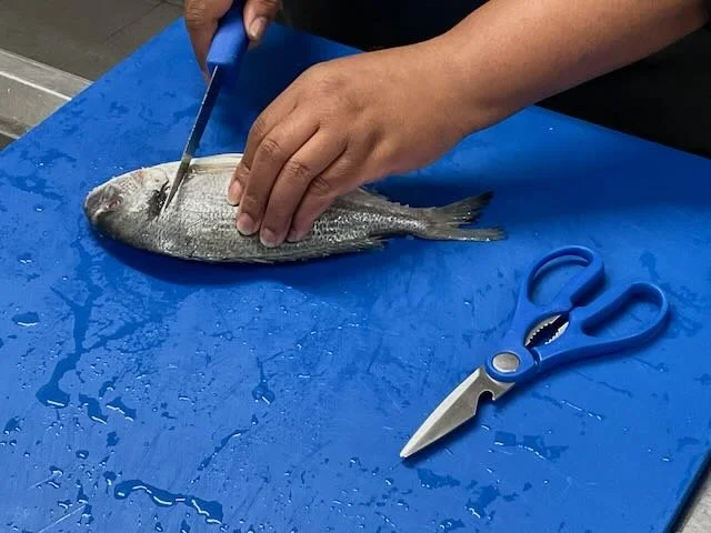  …to a CLOSE-UP of the FISHMONGER’S KNIFE as she expertly FILLETS the FISH.  CUT… 