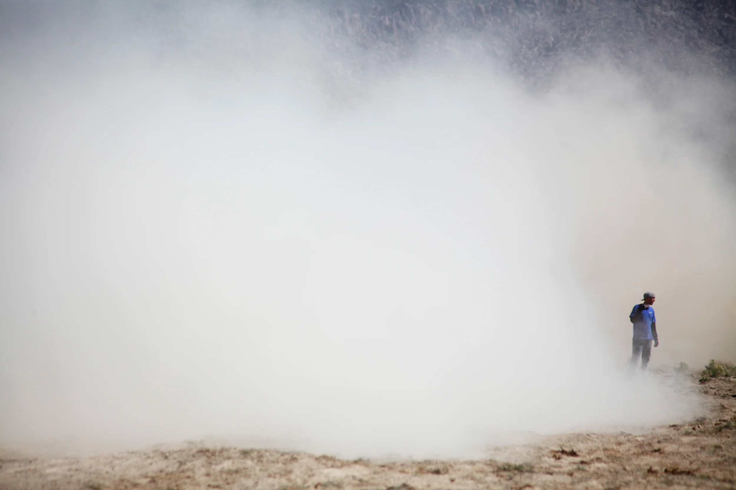  A cameraman turns his back as a cloud of dust envelopes him from passing race vehicles.&nbsp; 