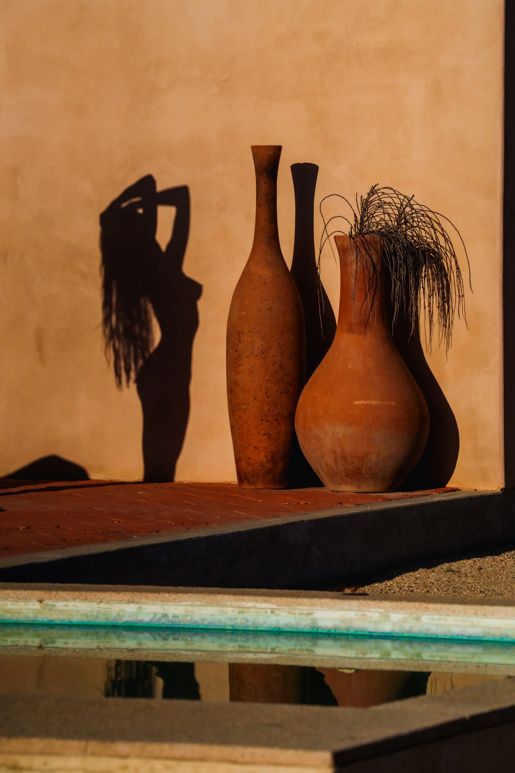 Three ceramic vases of varying shapes and sizes on a shelf, with their shadows cast on the wall behind them, creating abstract patterns.