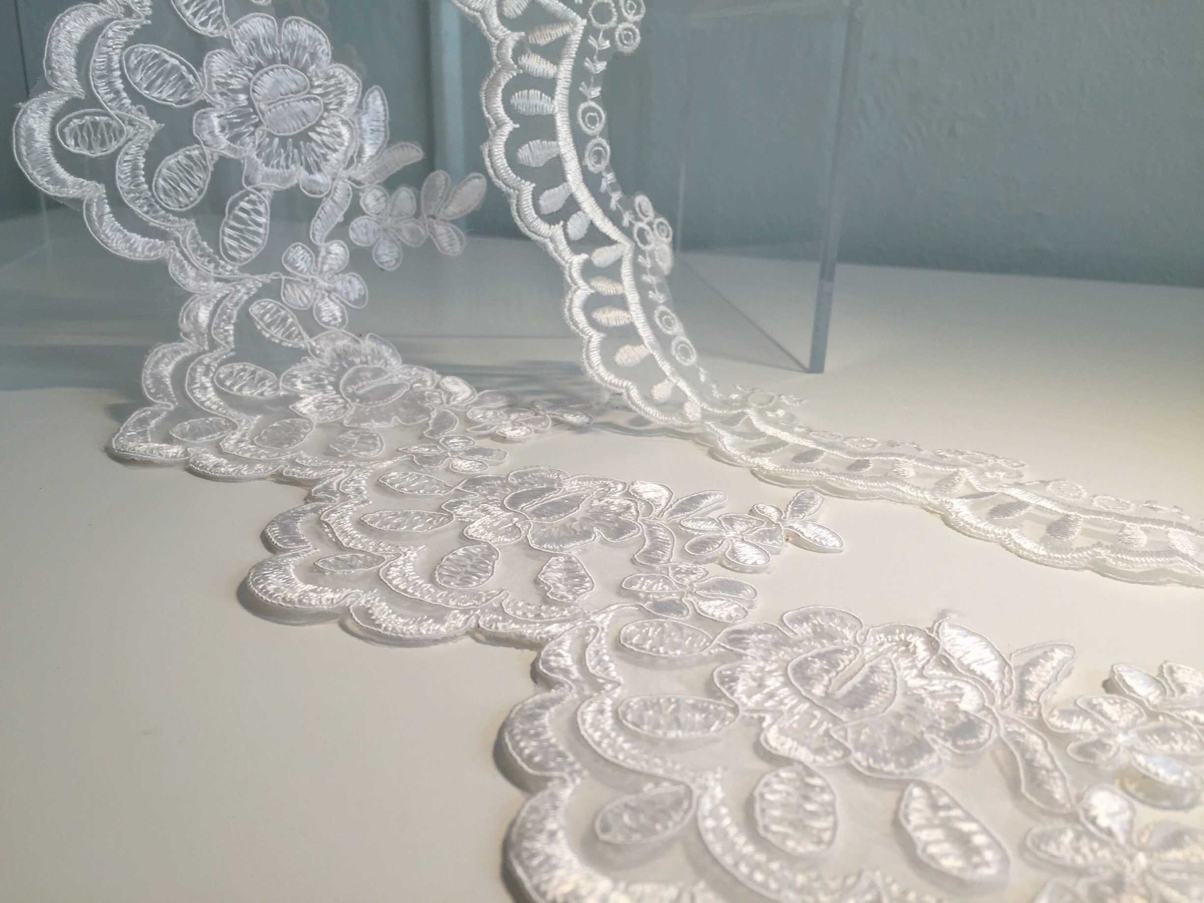 Embroidered Organza: Often used as a trim or an applique, embroidered organzas are machine made laces that can have a combination of features of traditionally handmade laces, but on the more stable and durable organza fabric ground instead of a fine mesh ground. Some have cording outlining the motifs like alençon lace, like that in the foreground here. These are often beaded or embellished and used for belts and bridal accessories. 