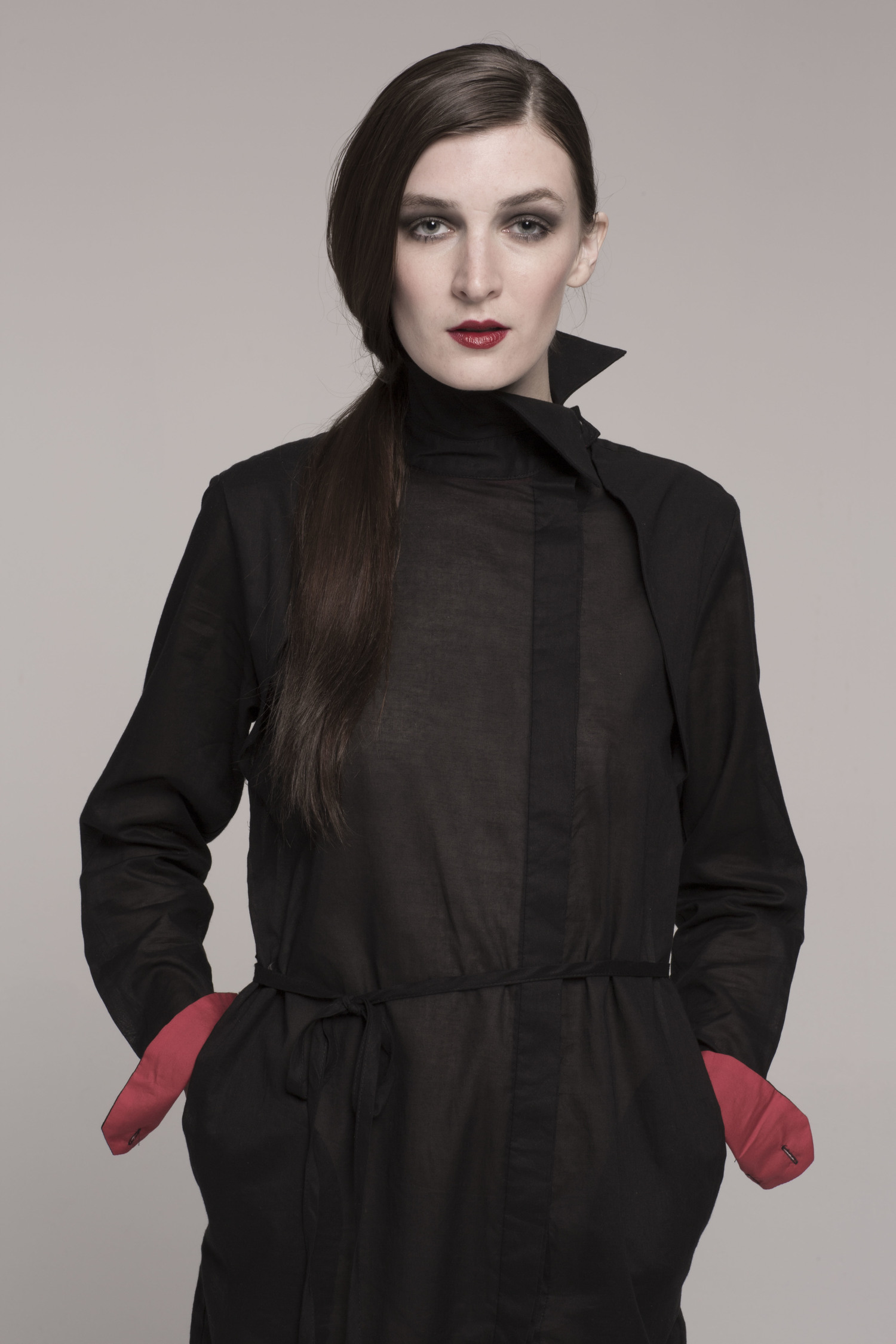 model, hands in pockets, in sheer black dress with red cuffs