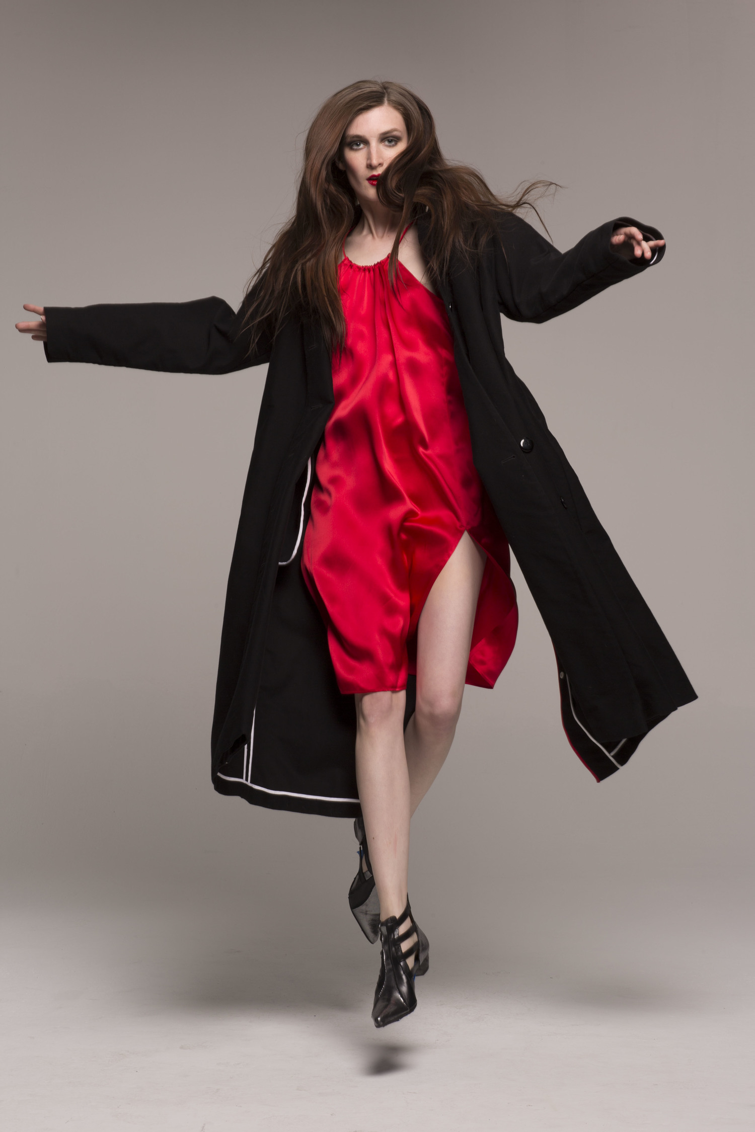model in red silk strap dress; jumping, wearing long black coat with flaps over dress