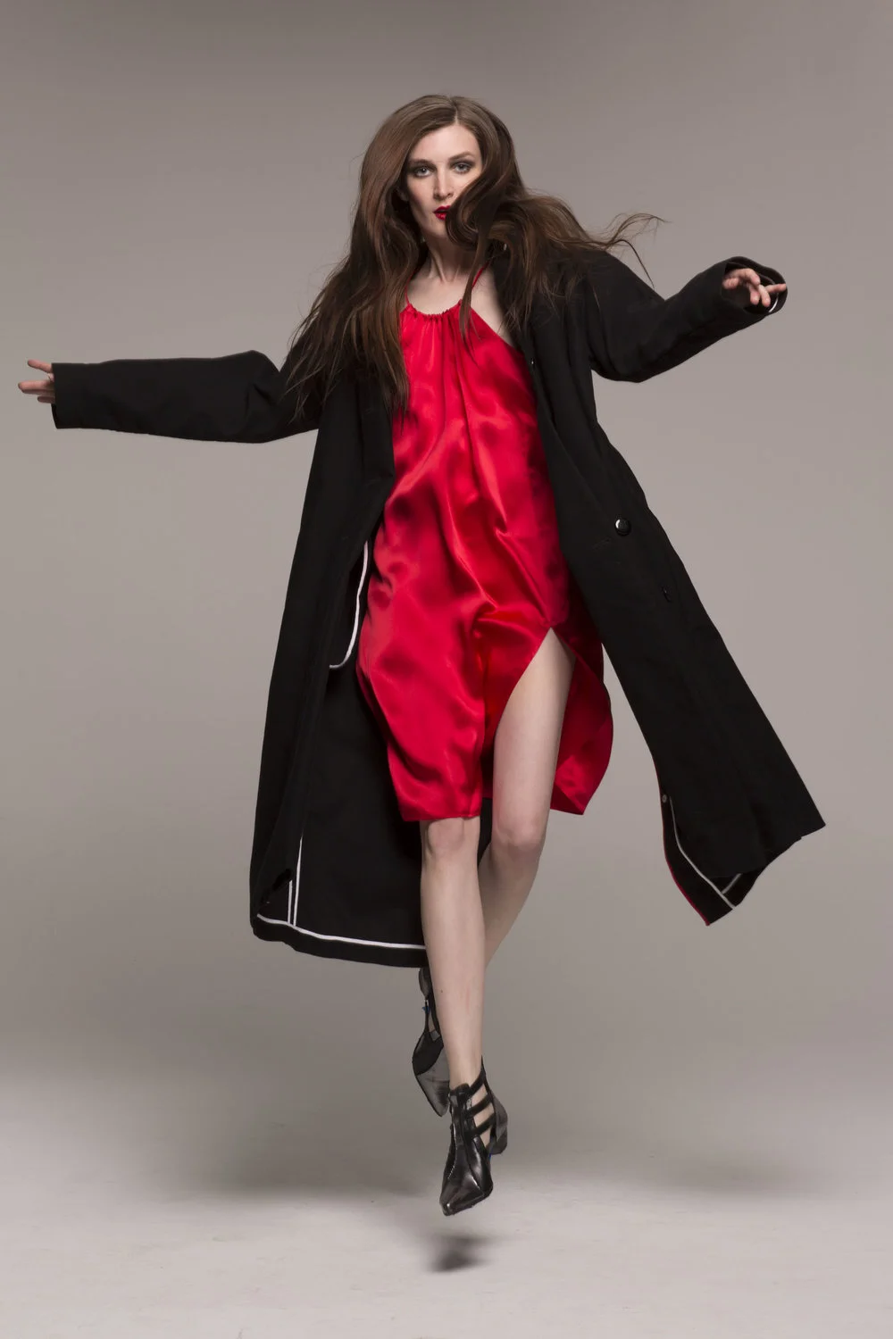 Model wearing red silk strap dress under long black coat