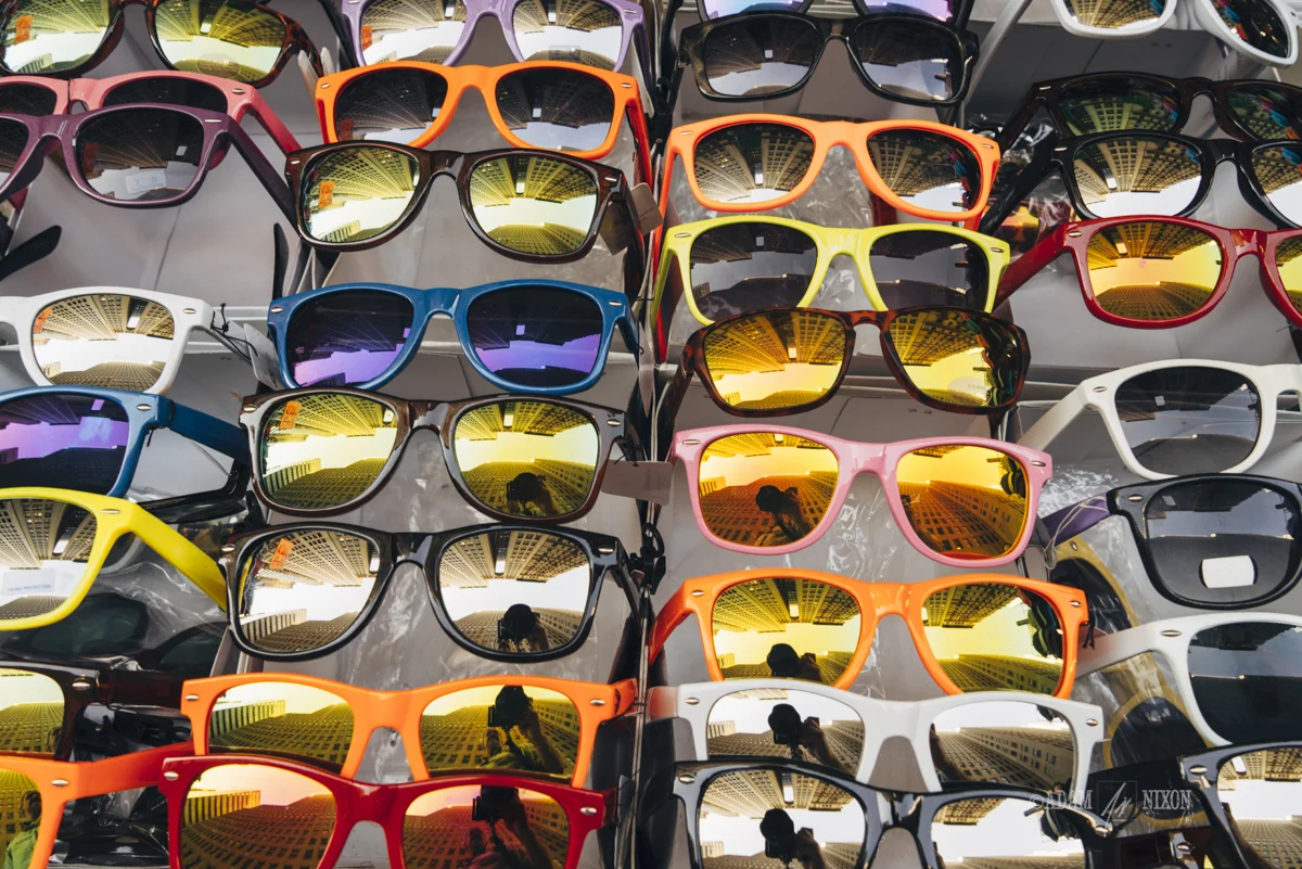 Street vendor display of colorful sunglasses with a reflection o