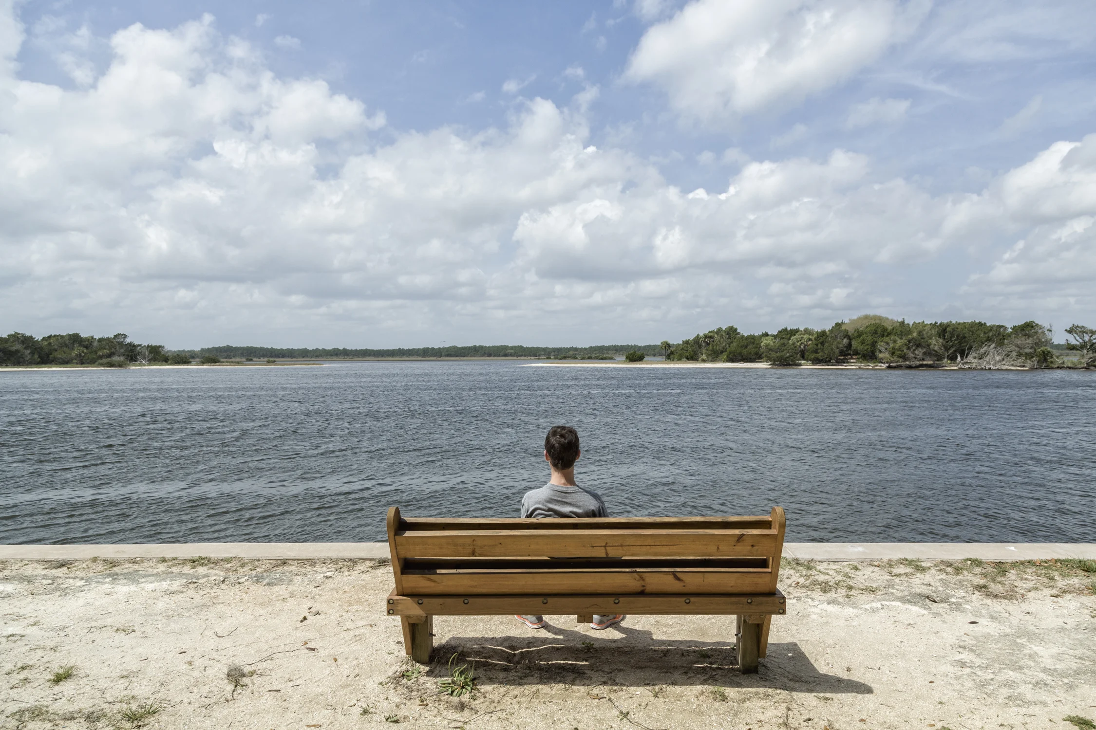 Teenage boy sitting on a wood bench looking out the water