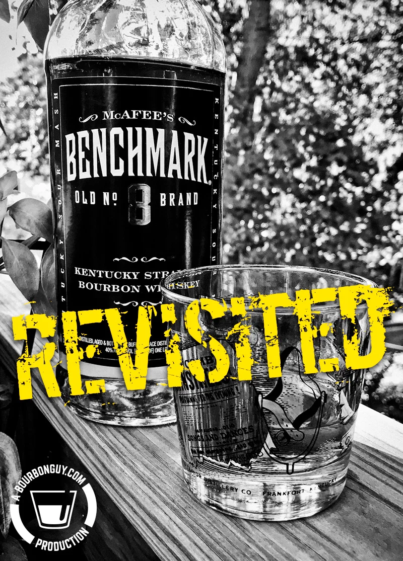 IMAGE: A bottle of Benchmark Bourbon, from the front with a glass beside it. Flanked by leaves.