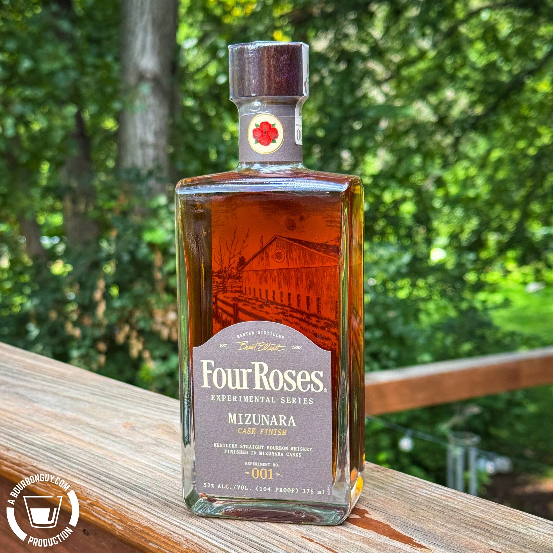 IMAGE: A bottle of Four Roses Experimental Series Experiment No. 001 Mizunara Cask Finish bourbon sits on a wooden deck railing against a softly blurred green background.
