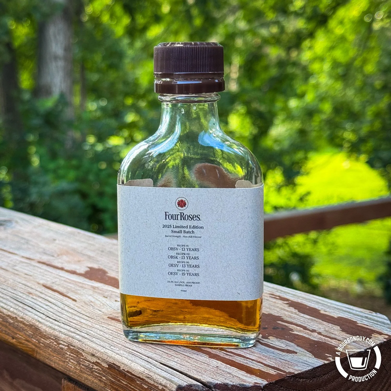 IMAGE: A sample bottle of Four Roses 2025 Limited Edition Small Batch bourbon sits on a wooden deck rail, surrounded by lush greenery in the background. Label lists four 13–19 year recipes.