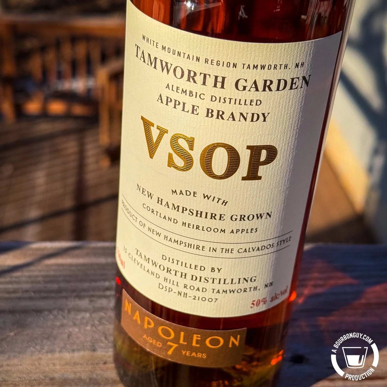 IMAGE: Tamworth Garden VSOP Apple Brandy bottle, 7-year Napoleon, 50% ABV, made with NH Cortland heirloom apples, Calvados style, on an outdoor wooden surface.
