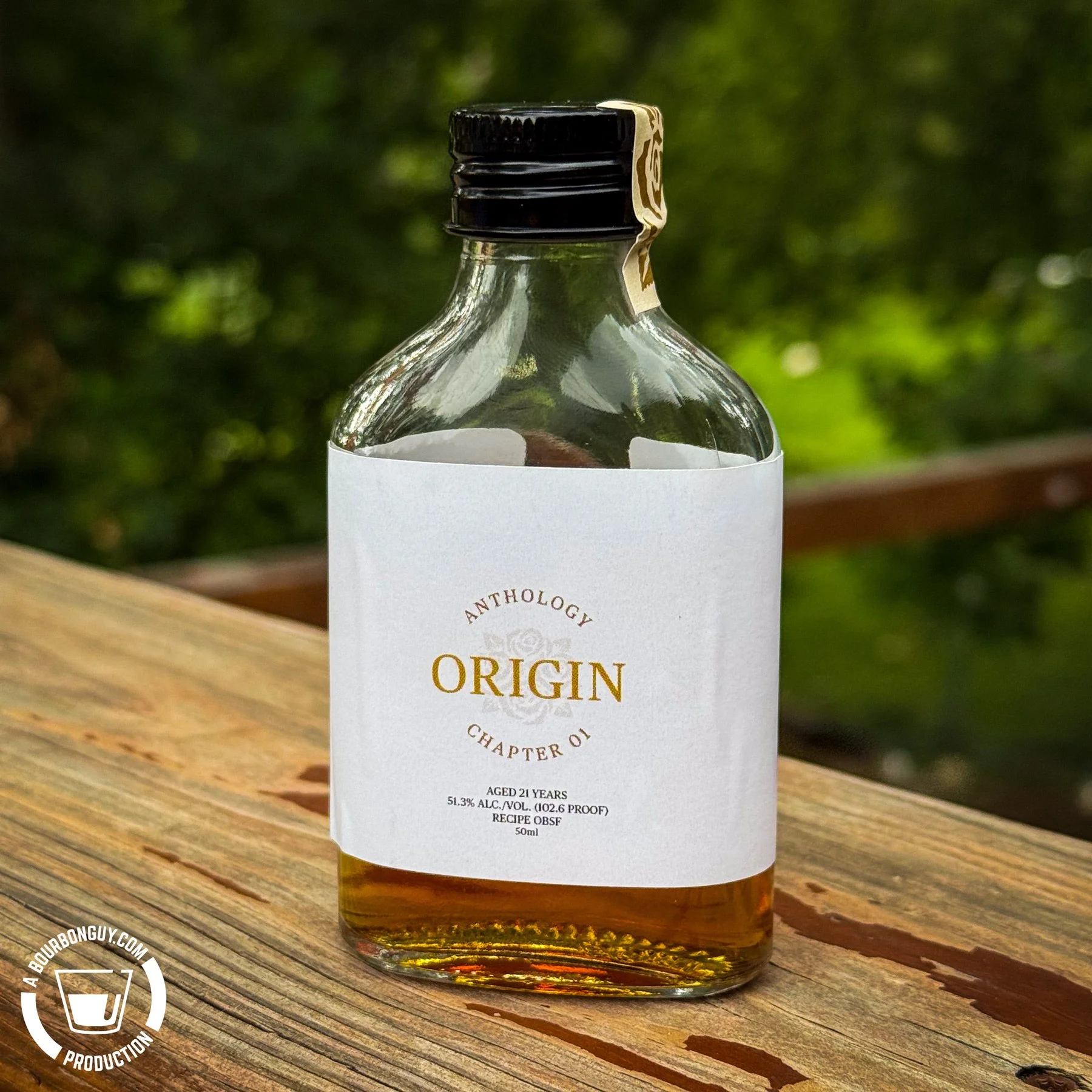 IMAGE: A sample bottle of Four Roses Anthology Origin Chapter 01, a 21-year-old bourbon, sits on a wooden deck railing against a softly blurred green background.