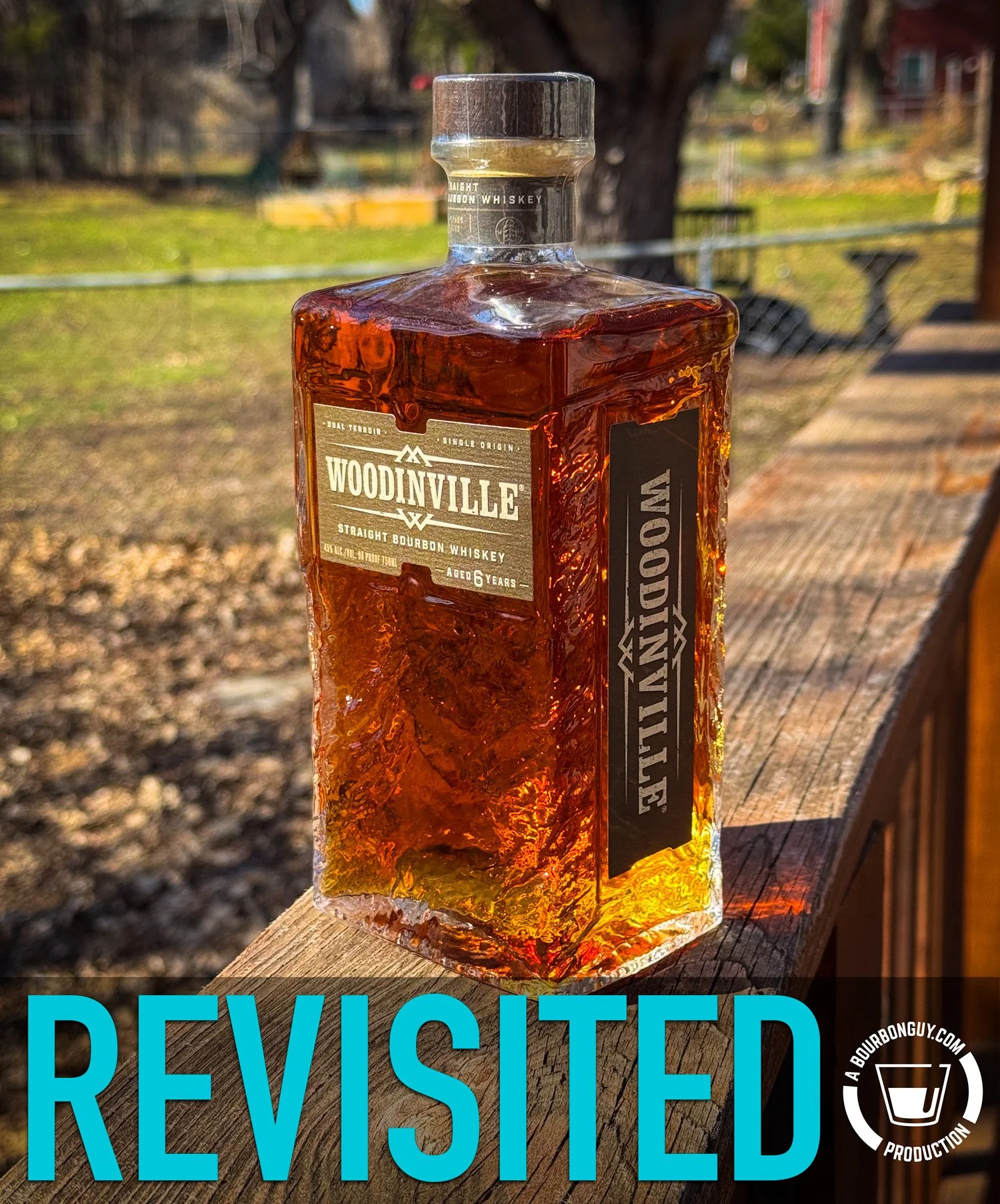 IMAGE: Woodinville Straight Bourbon Whiskey bottle (aged 6 years) on a sunlit wooden deck with backyard in the background; large “REVISITED” text overlays the bottom with a BourbonGuy watermark in the corner