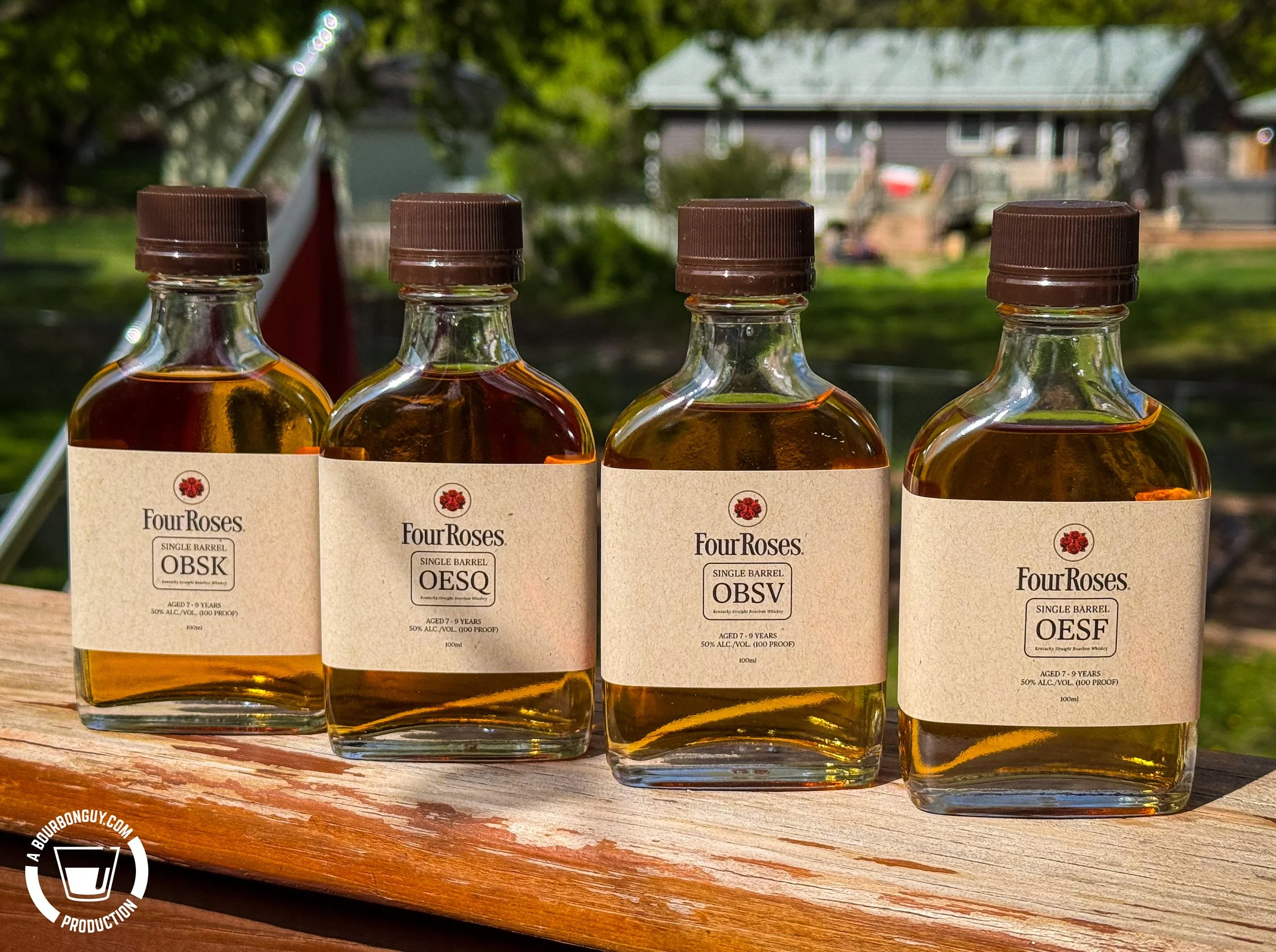 IMAGE: Four sample bottles of Four Roses Single Barrel bourbon recipes OBSK, OESQ, OBSV, and OESF lined up on a deck railing outdoors on a sunny morning.