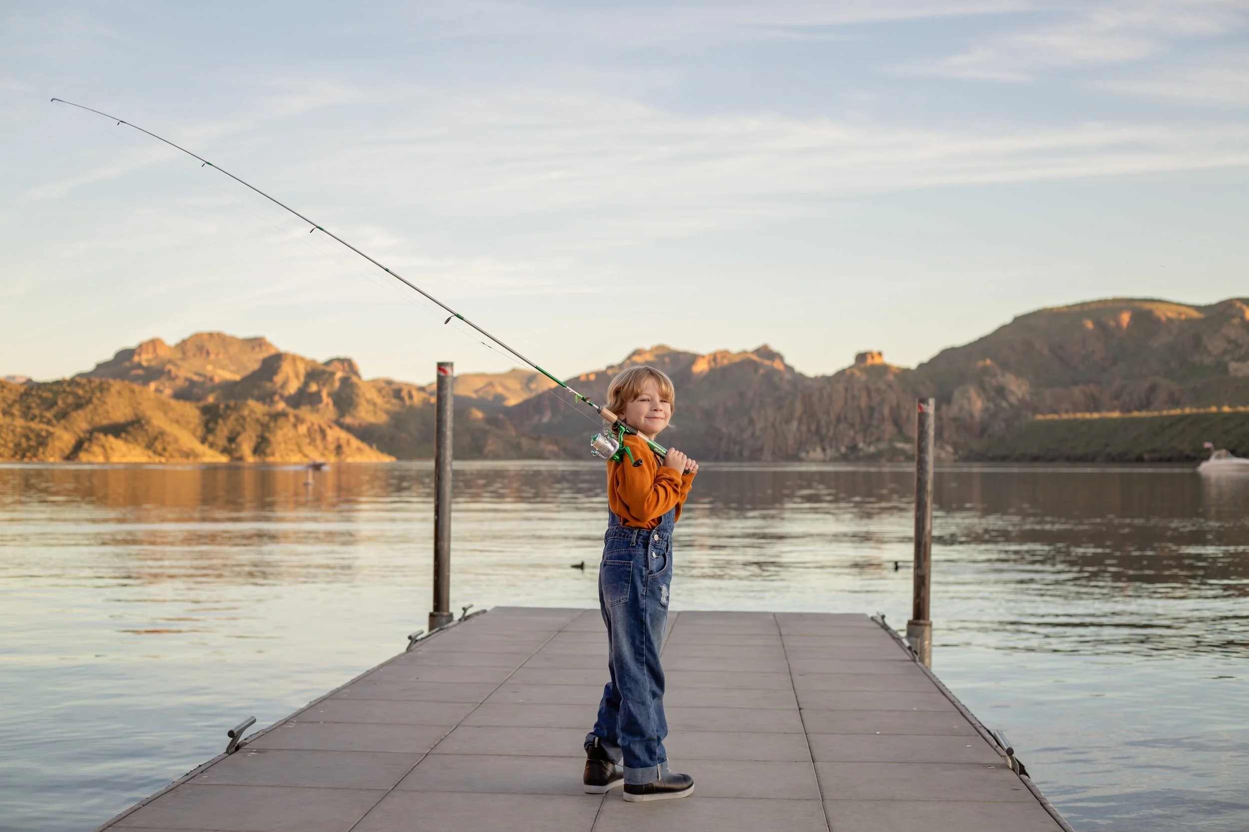 Child sitting on a dock holding a fishing pole and watching the water at sunset in Arizona, photographed by a Gilbert family photographer