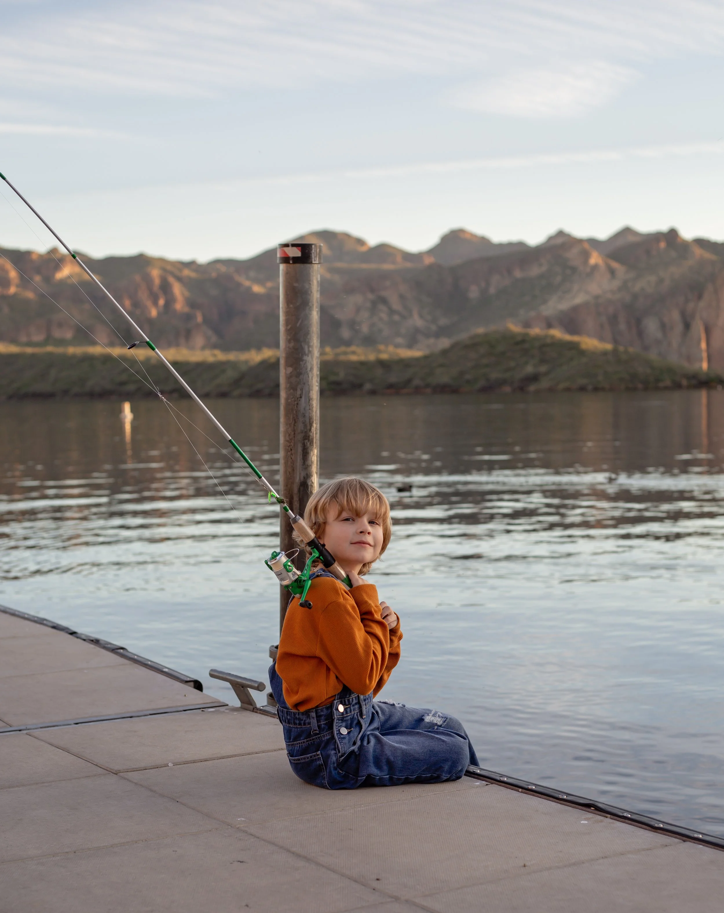 Child sitting on a dock holding a fishing pole and watching the water at sunset in Arizona, photographed by a Gilbert family photographer
