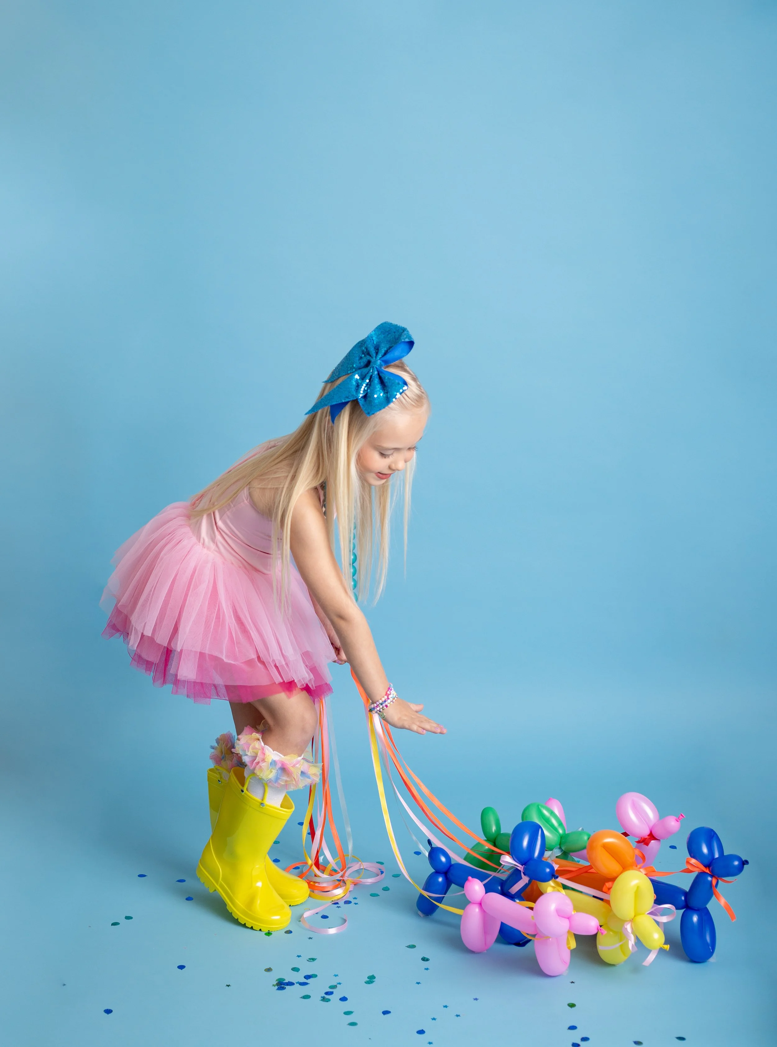 Joyful birthday portrait of a young girl with a balloon dog on a blue backdrop, photographed by a Gilbert, Arizona child photographer.