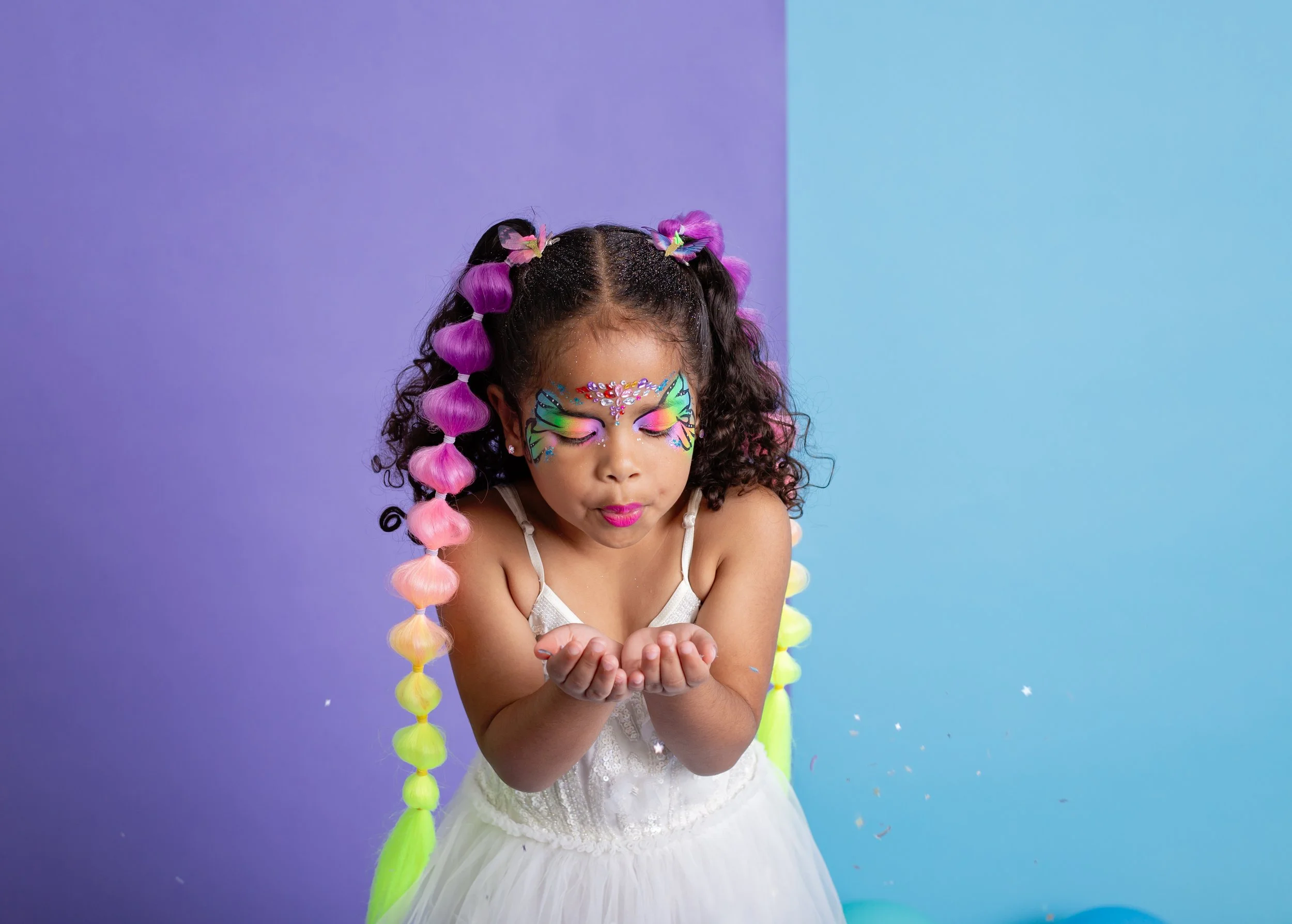 young girls with colorful braided hair extensions and vibrant animal face paint sit together during a studio branding session for an East Valley Arizona face painter, photographed by a Gilbert Arizona child photographer.