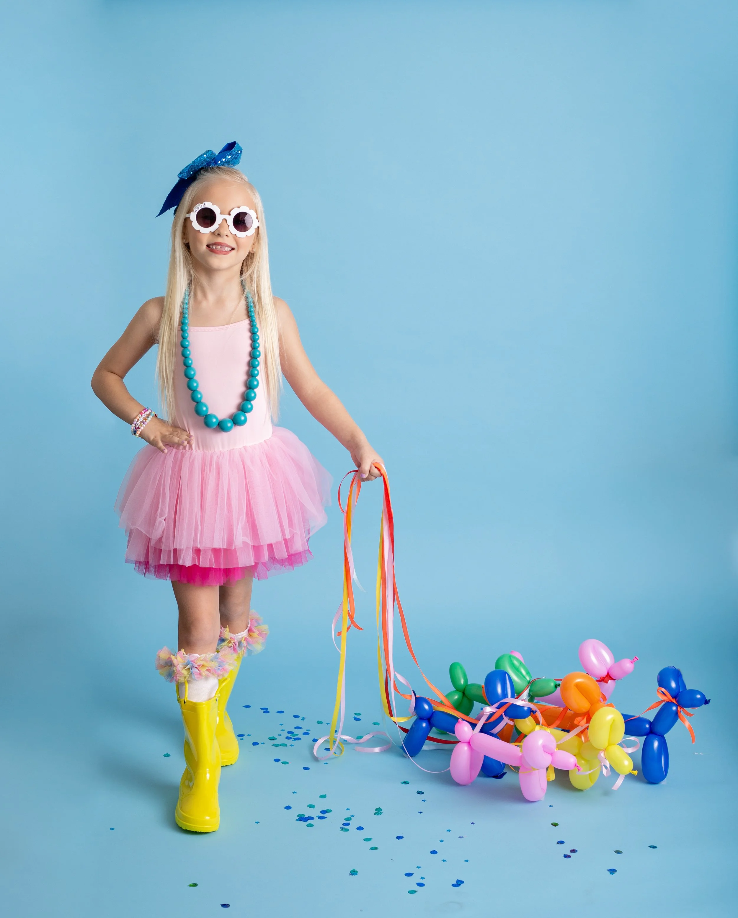 Playful kids birthday photography in Gilbert, Arizona featuring a girl posing with a rainbow balloon dog.