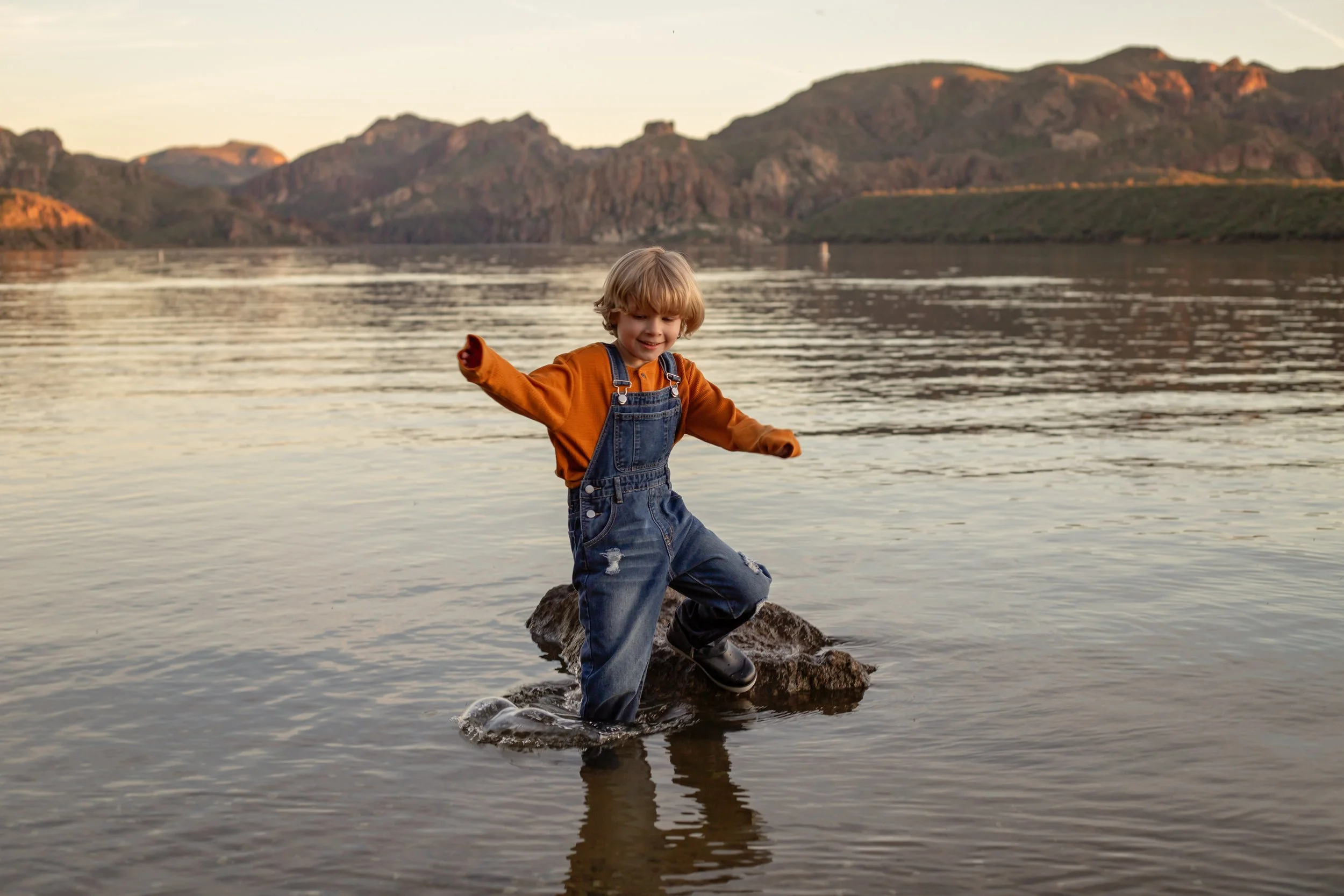 Child sitting on a dock holding a fishing pole and watching the water at sunset in Arizona, photographed by a Gilbert family photographer