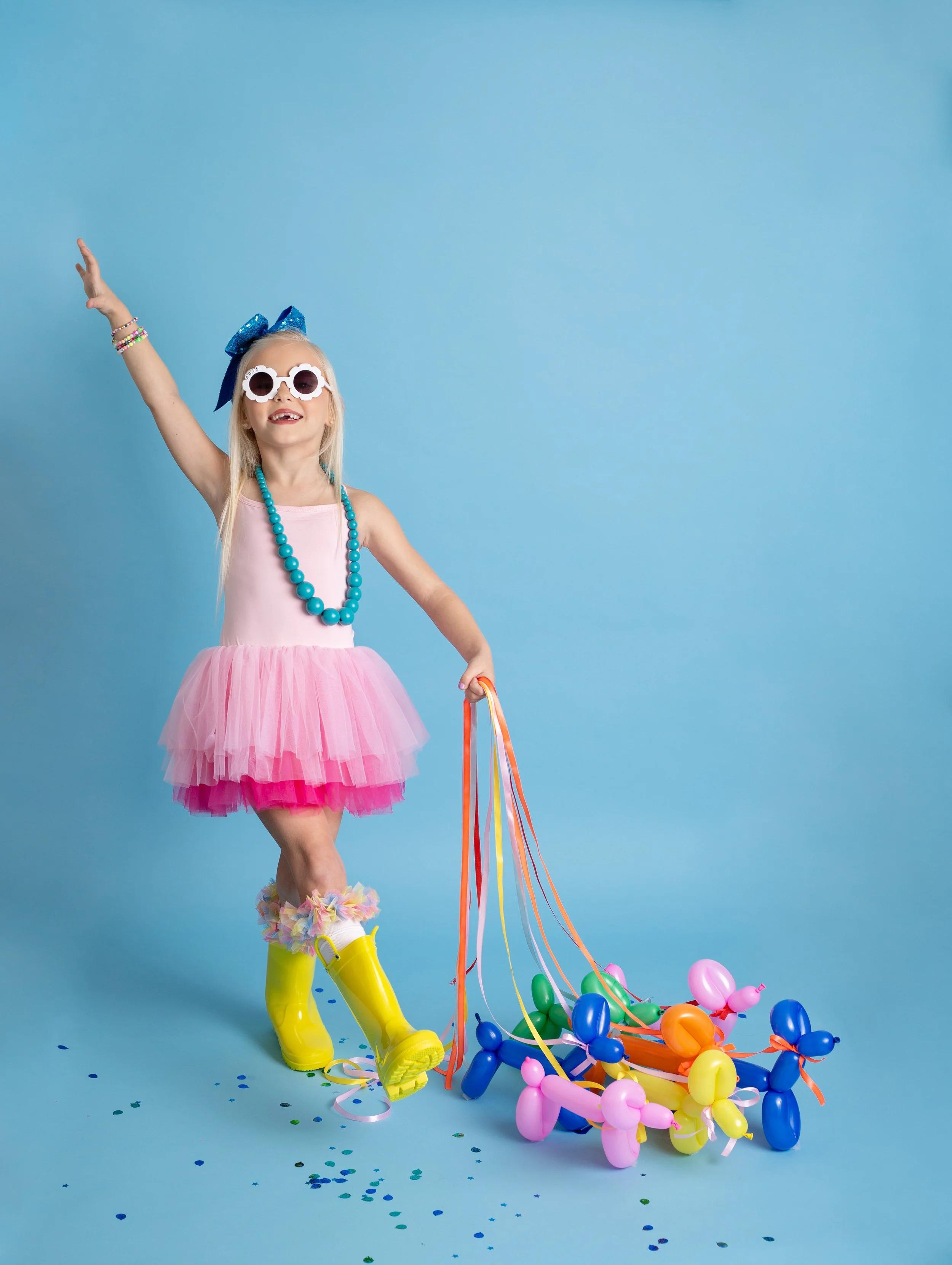 Playful kids birthday photography in Gilbert, Arizona featuring a girl posing with a rainbow balloon dog.