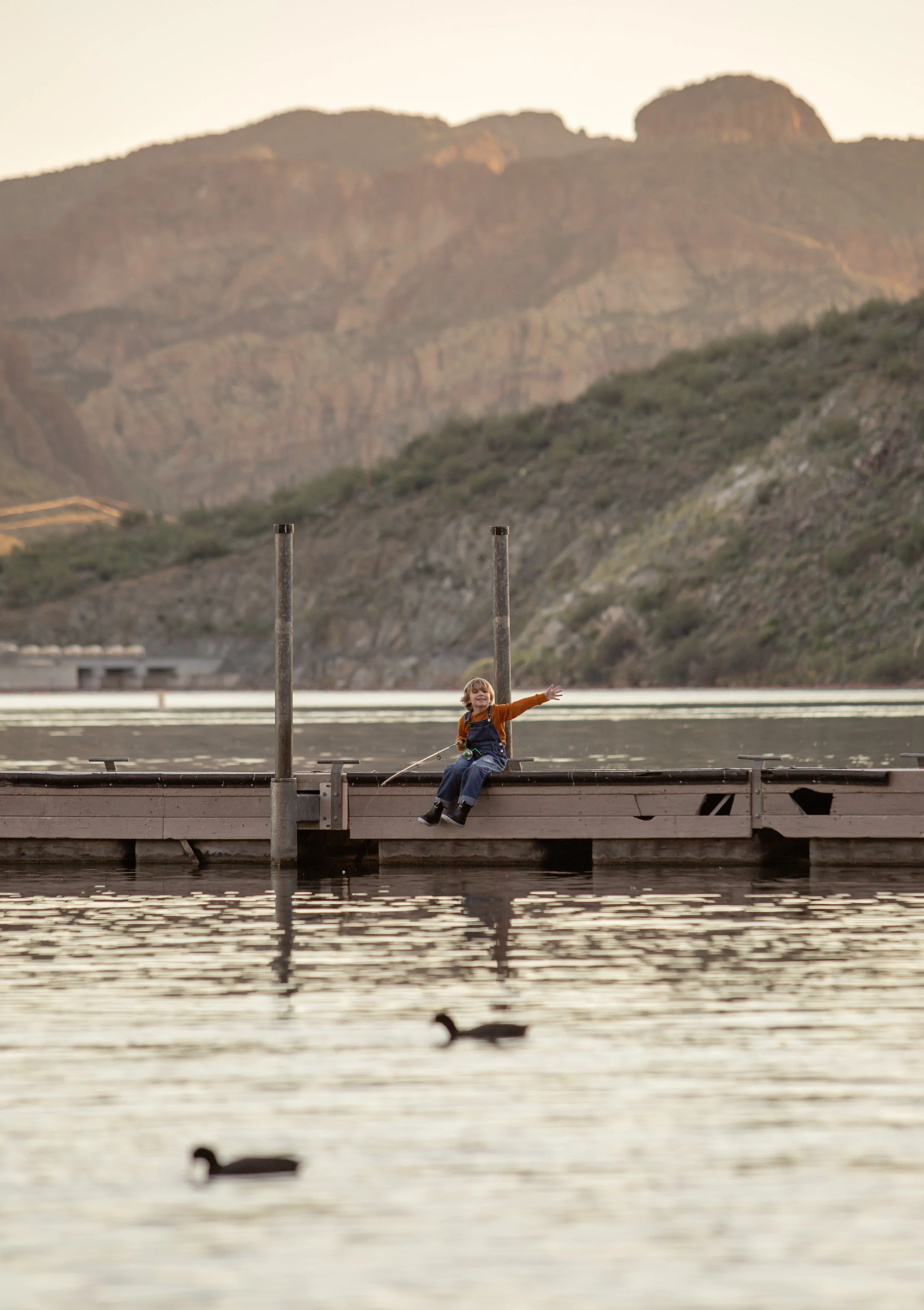 Child sitting on a dock holding a fishing pole and watching the water at sunset in Arizona, photographed by a Gilbert family photographer