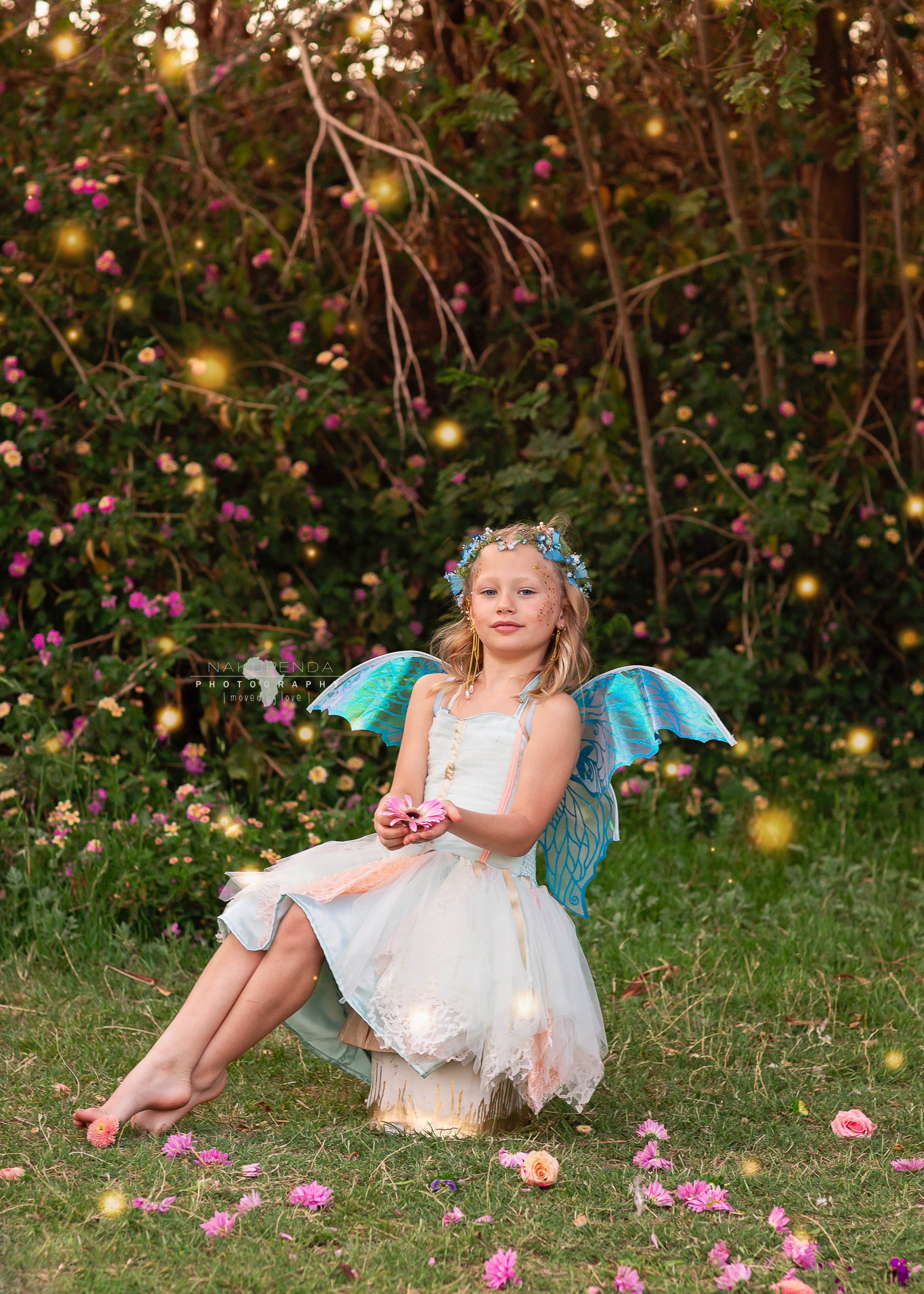 Young girls dressed as fairies in pastel dresses and wings sitting in a magical outdoor meadow with oversized mushrooms and flower crowns, captured during an enchanted fairy photo session by a child photographer in Gilbert, Arizona.