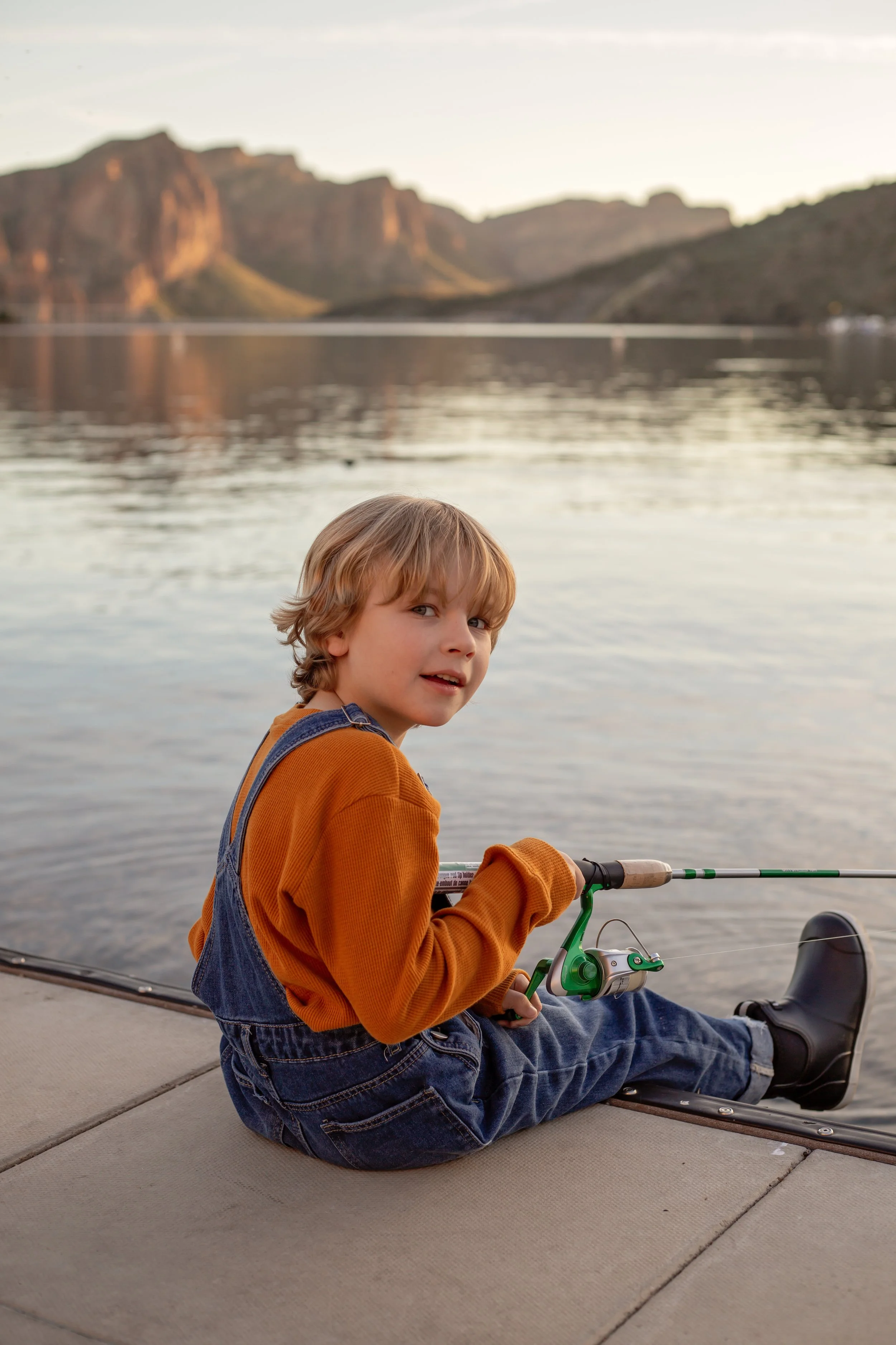 Child sitting on a dock holding a fishing pole and watching the water at sunset in Arizona, photographed by a Gilbert family photographer