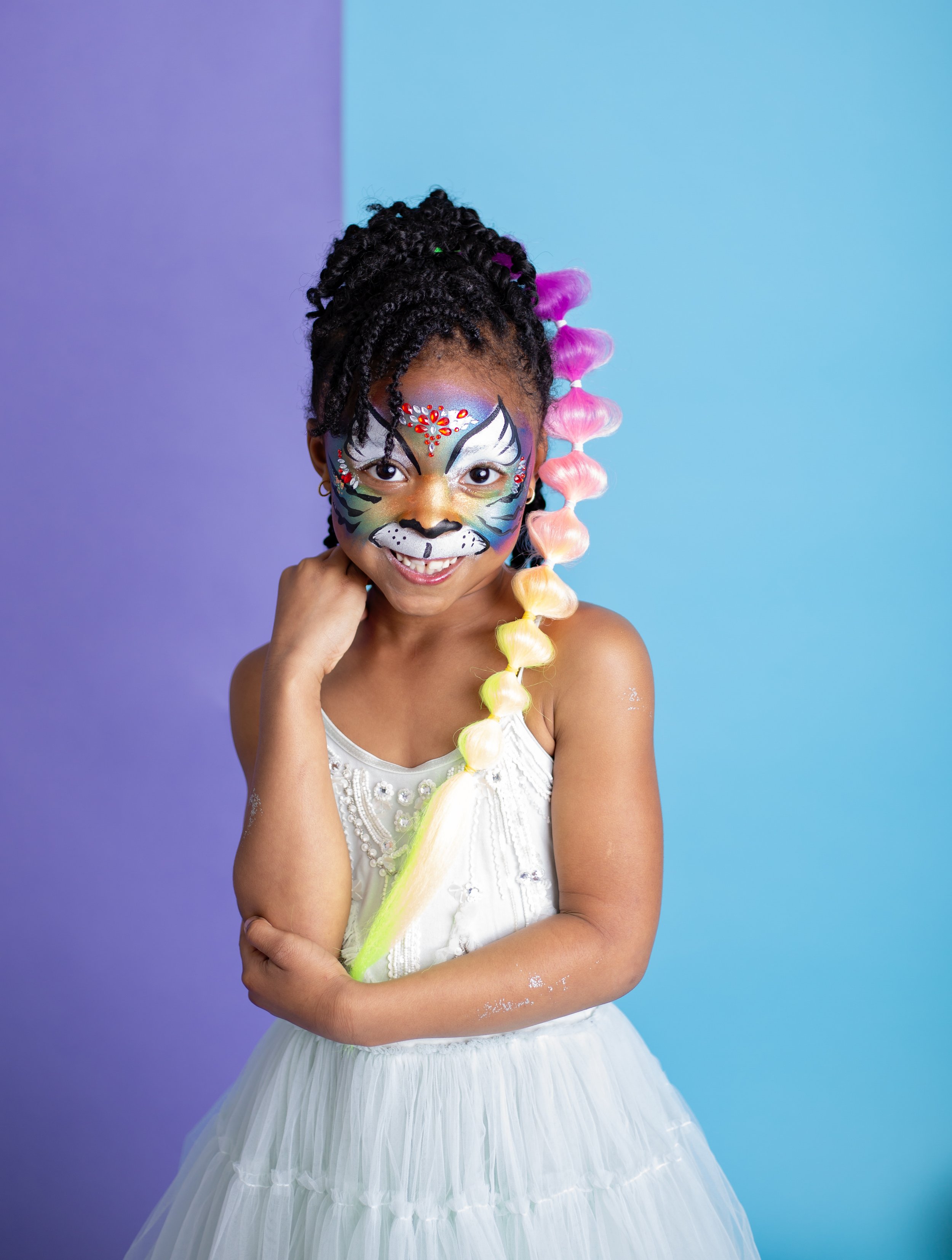 young girls with colorful braided hair extensions and vibrant animal face paint sit together during a studio branding session for an East Valley Arizona face painter, photographed by a Gilbert Arizona child photographer.