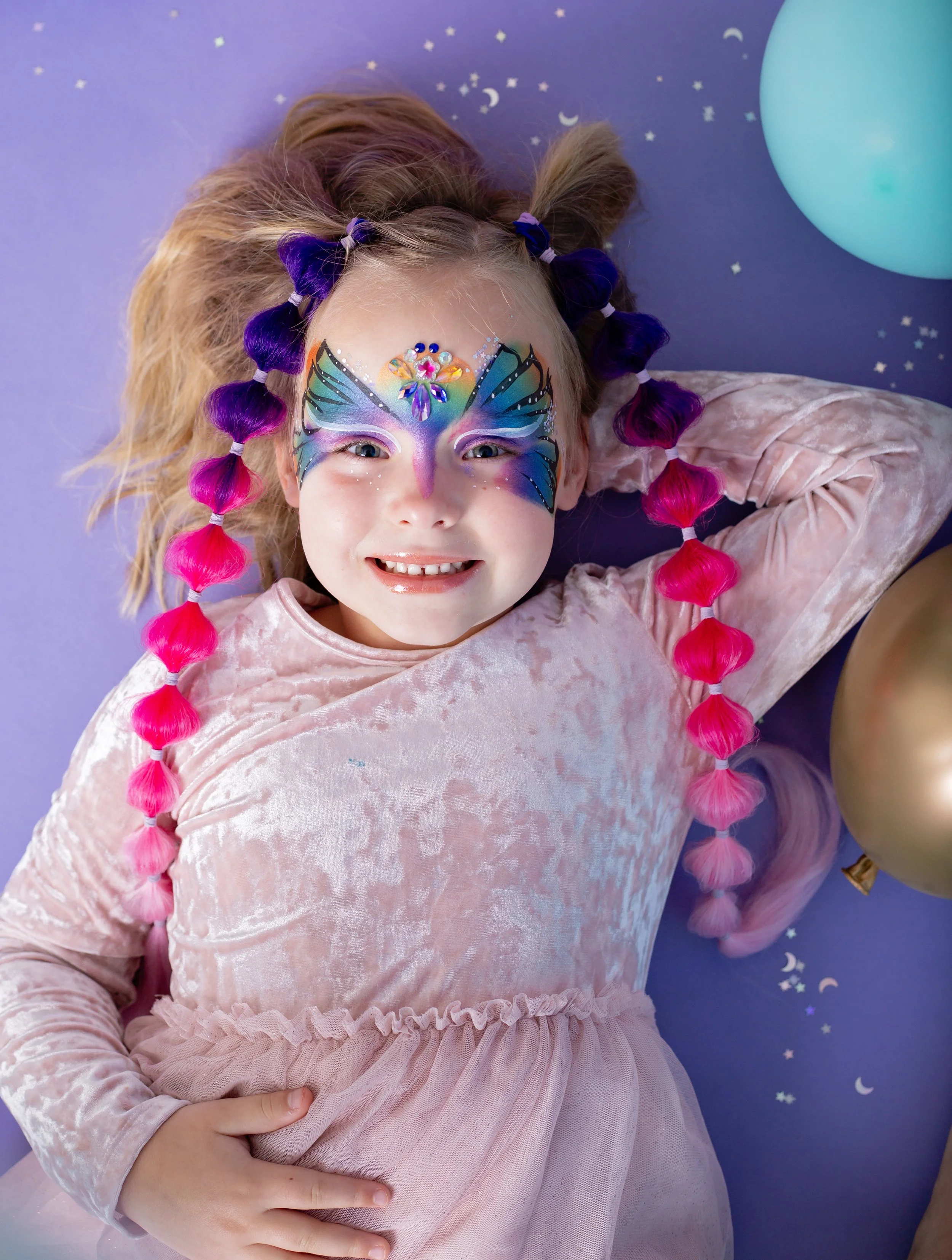young girls with colorful braided hair extensions and vibrant animal face paint sit together during a studio branding session for an East Valley Arizona face painter, photographed by a Gilbert Arizona child photographer.