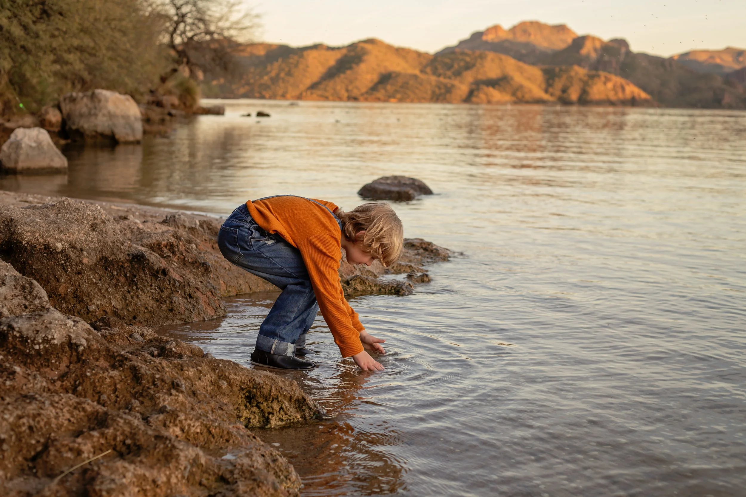 Child sitting on a dock holding a fishing pole and watching the water at sunset in Arizona, photographed by a Gilbert family photographer