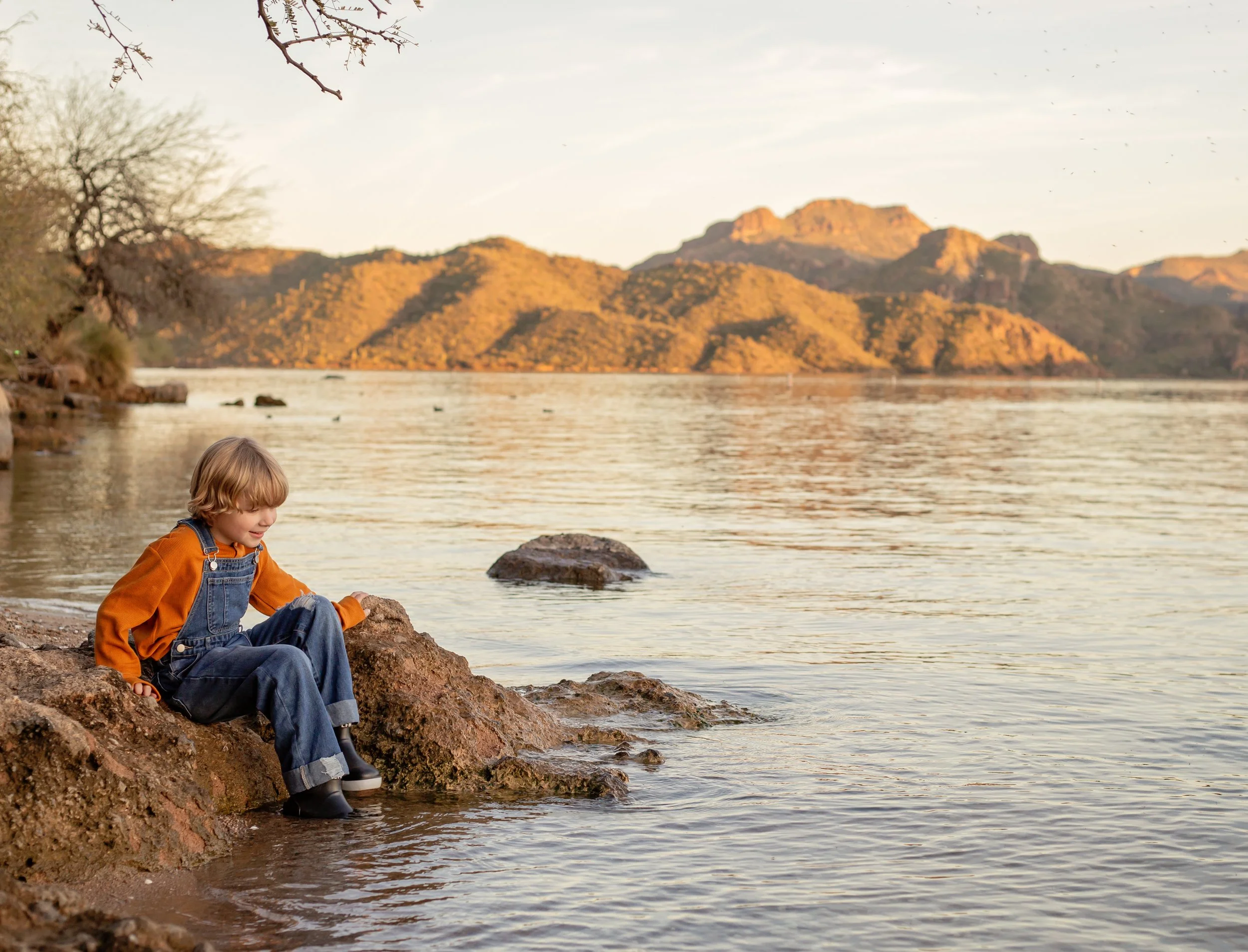 Child sitting on a dock holding a fishing pole and watching the water at sunset in Arizona, photographed by a Gilbert family photographer