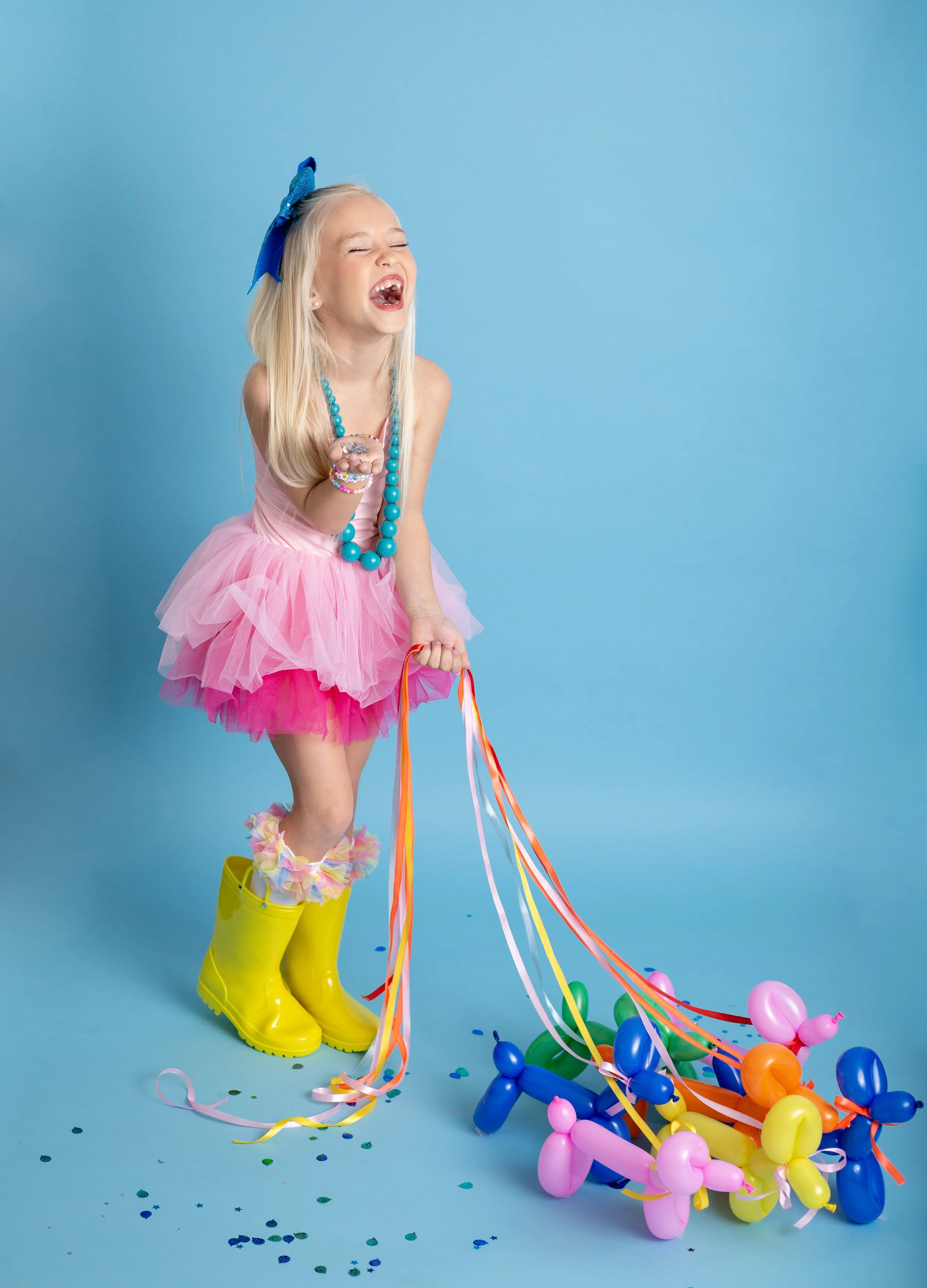 Joyful birthday portrait of a young girl with a balloon dog on a blue backdrop, photographed by a Gilbert, Arizona child photographer.