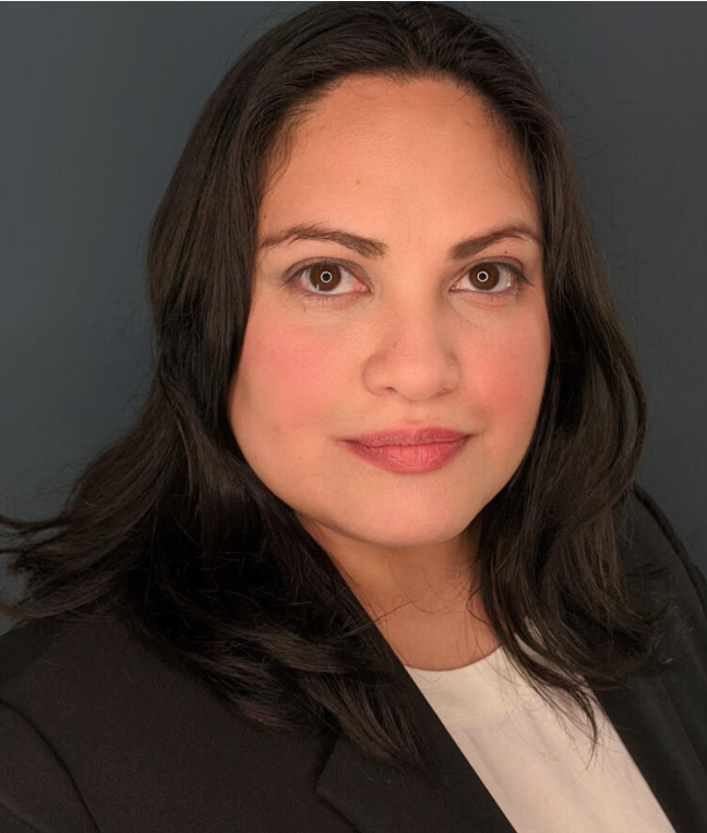 A portrait of a woman with dark brown hair, brown eyes, wearing a black blazer and white shirt against a gray background.