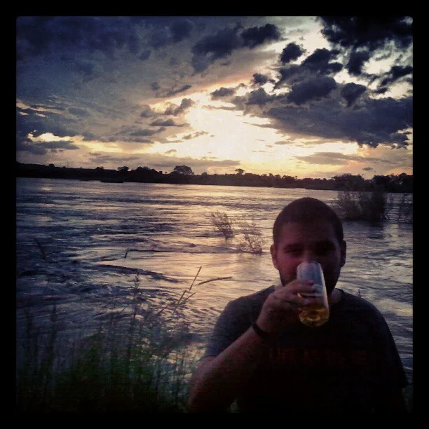 Me drinking a beer on the banks of the Zambezi river.