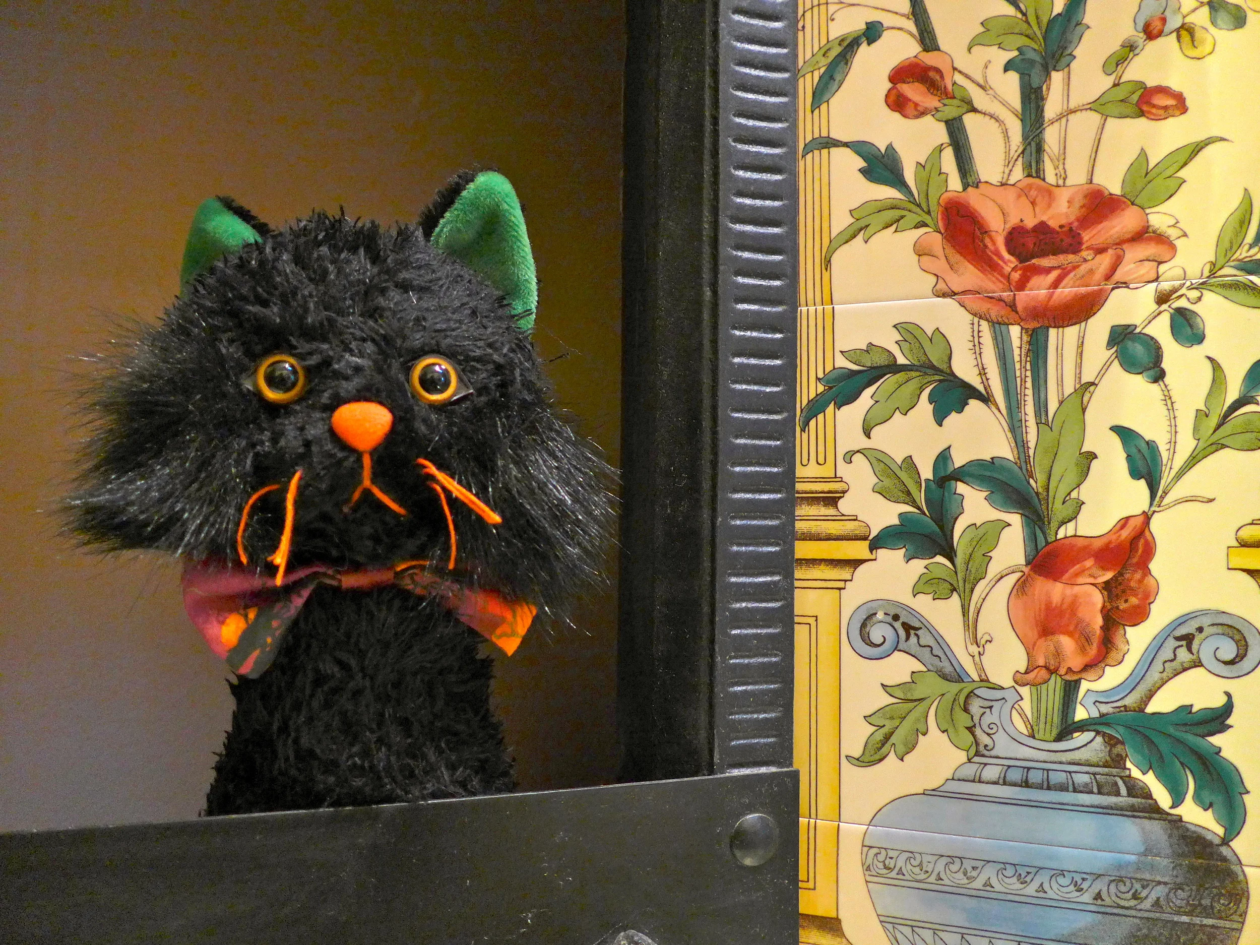 Black cat hand puppet next to Victorian floral tile fireplace surround