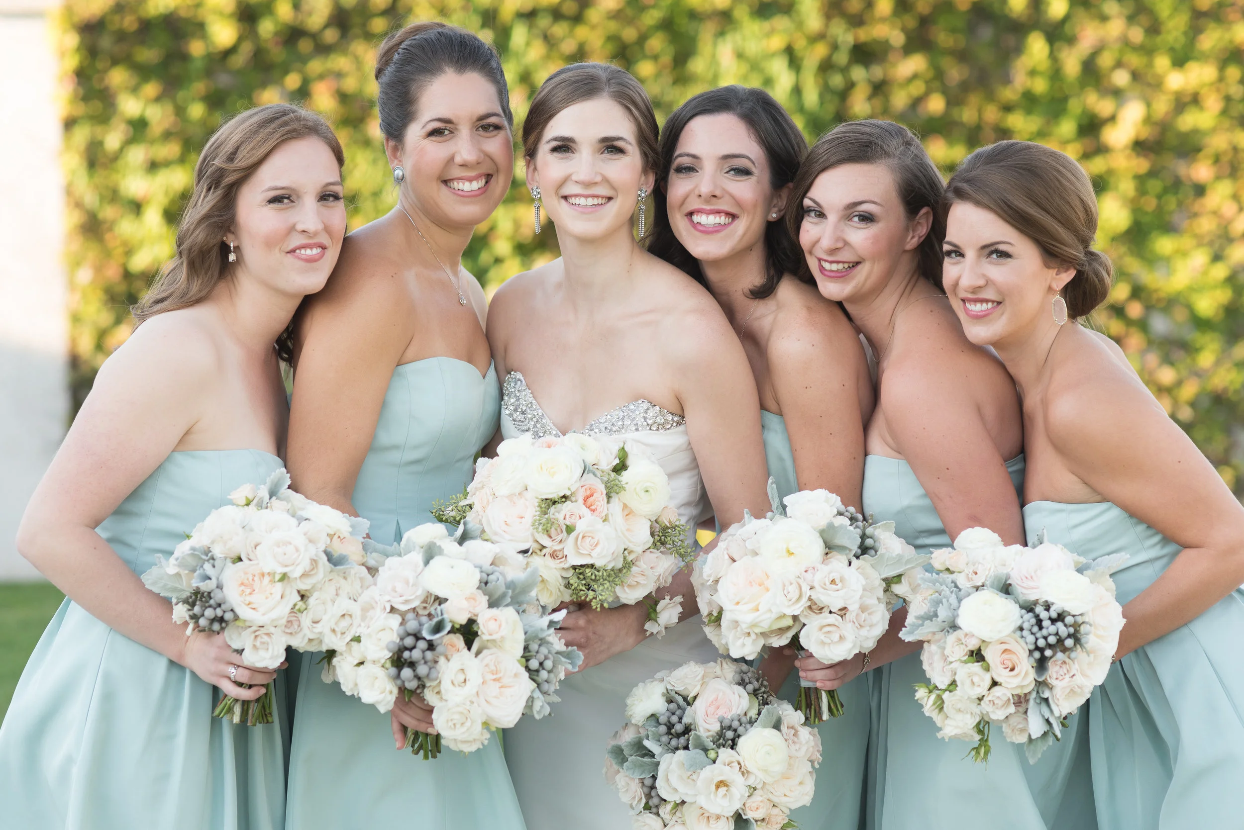 Bride between her bridesmaids dressed in light green in front of foliage in newport, rhode island