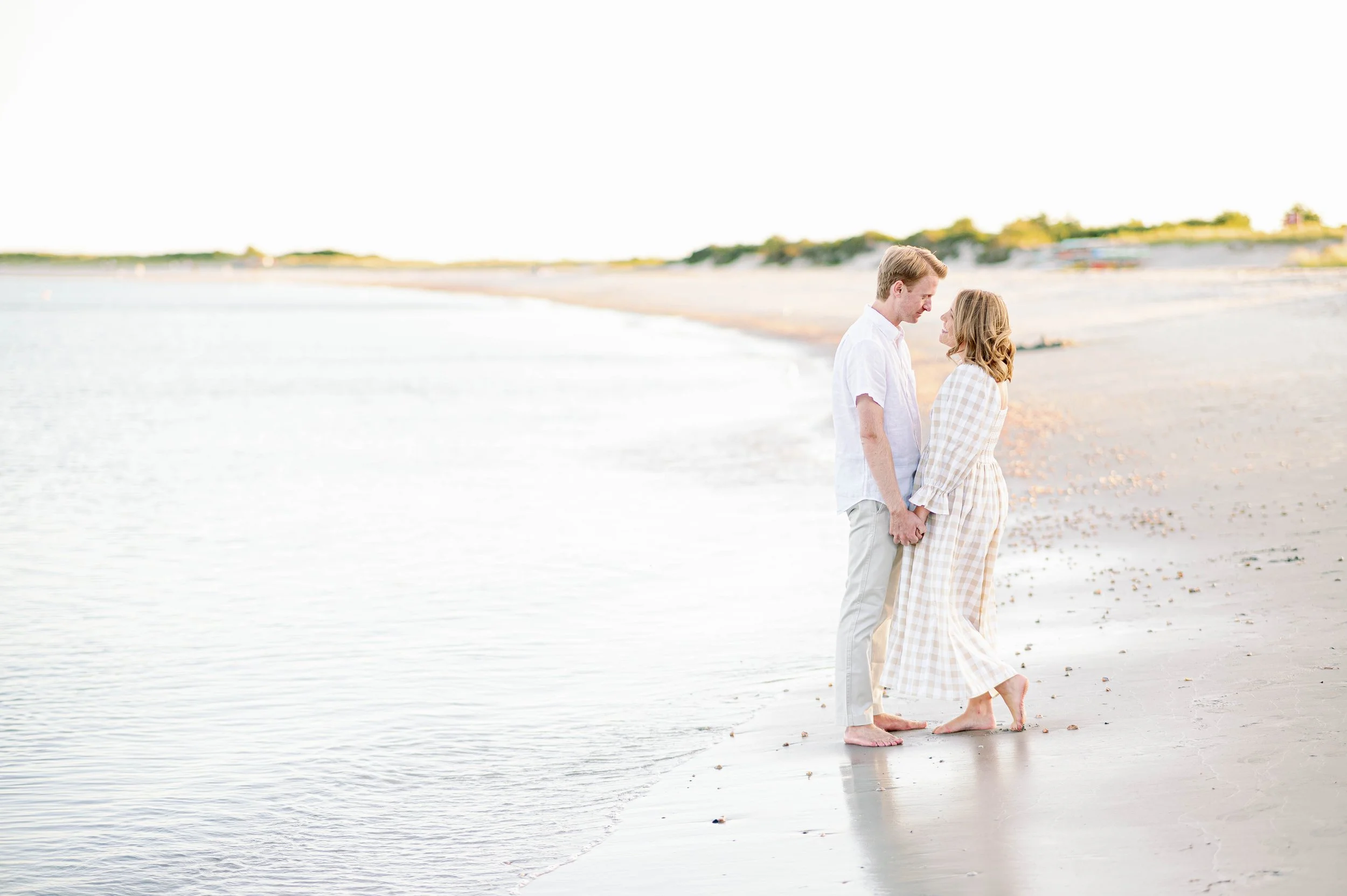 Engaged couple on sandy beach in Newport, RI at the water's edge for engagement photos.