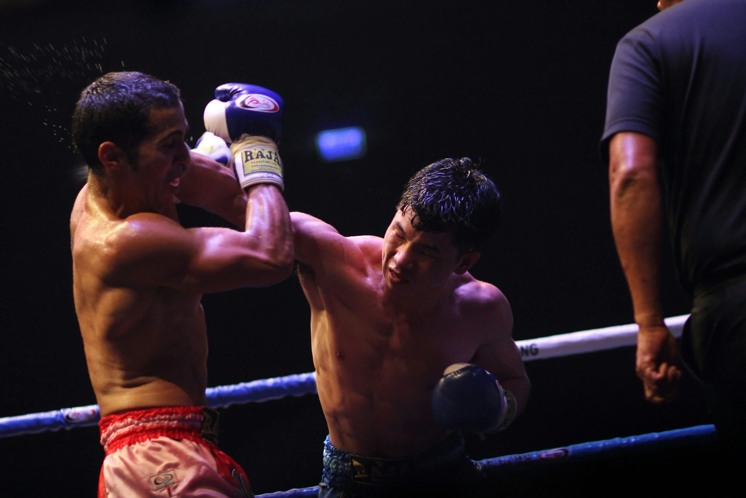 Two boxers in a ring, one is punching the other, who has his hands up in front of his face.