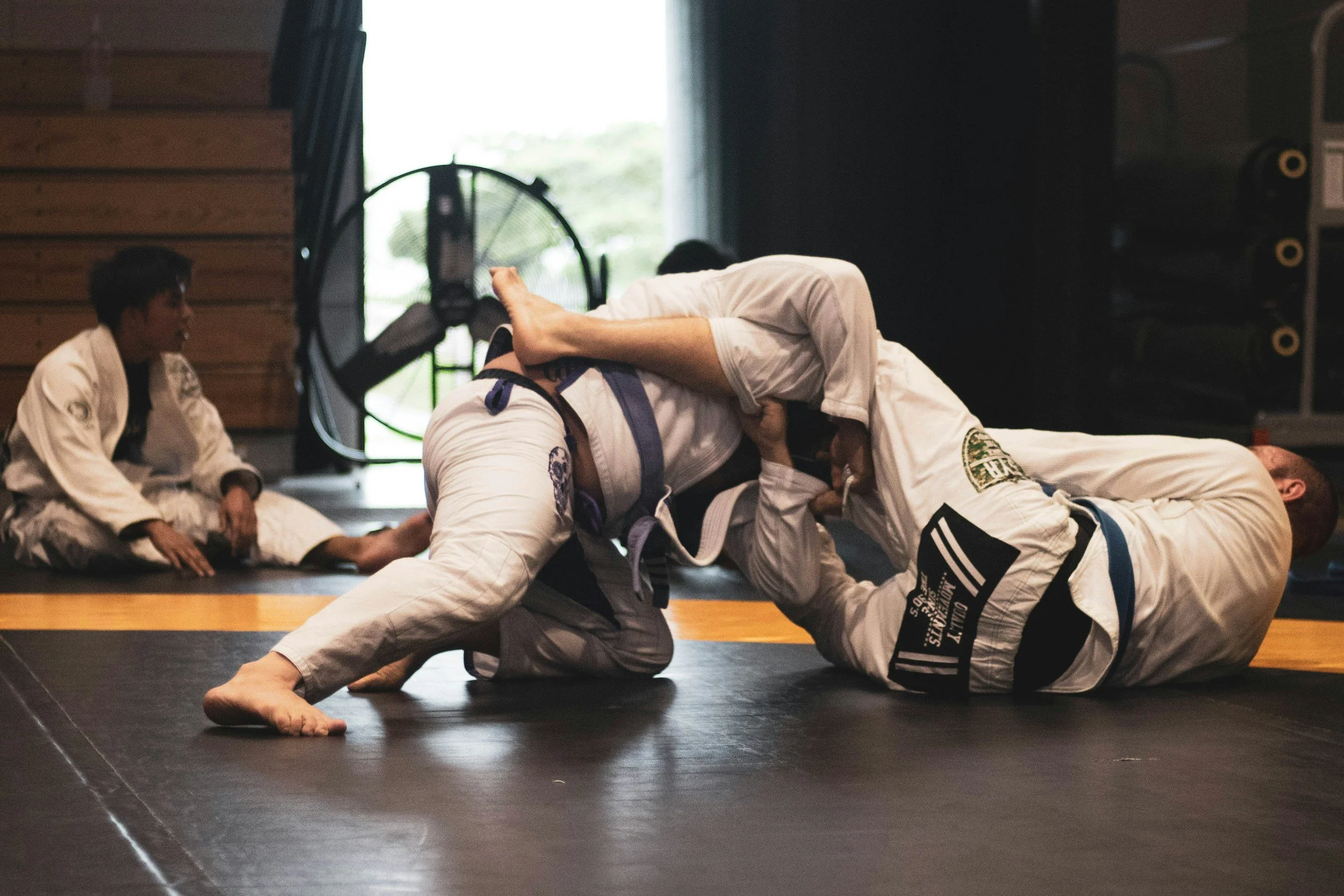 Two male gi jiu jitsu athletes on the mats in class
