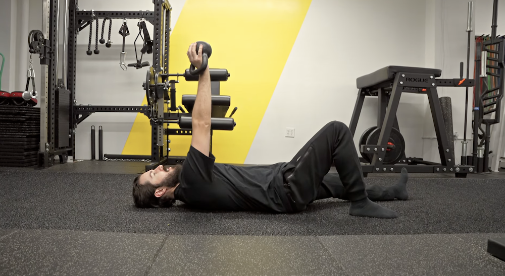 Coach Mark DiSalvo lying on his back on the turf at DiSalvo Performance Training, demonstrating a serratus punch with a small kettlebell