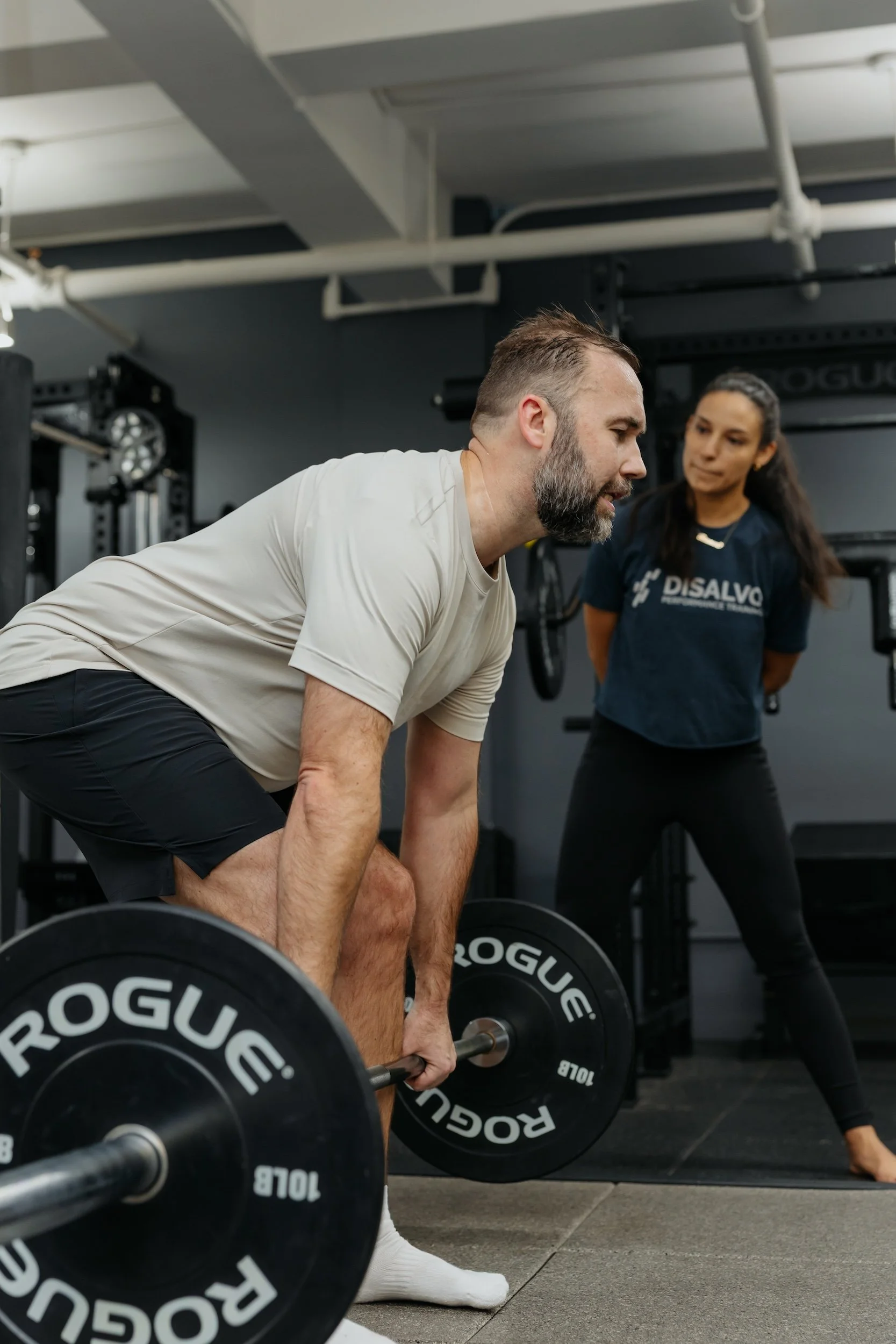 Male client doing bent over barbell rows with his trainer looking on at DiSalvo Performance Training
