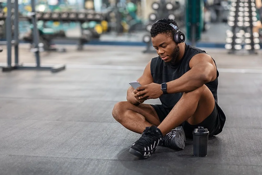 man sitting on the floor at the gym looking at phone