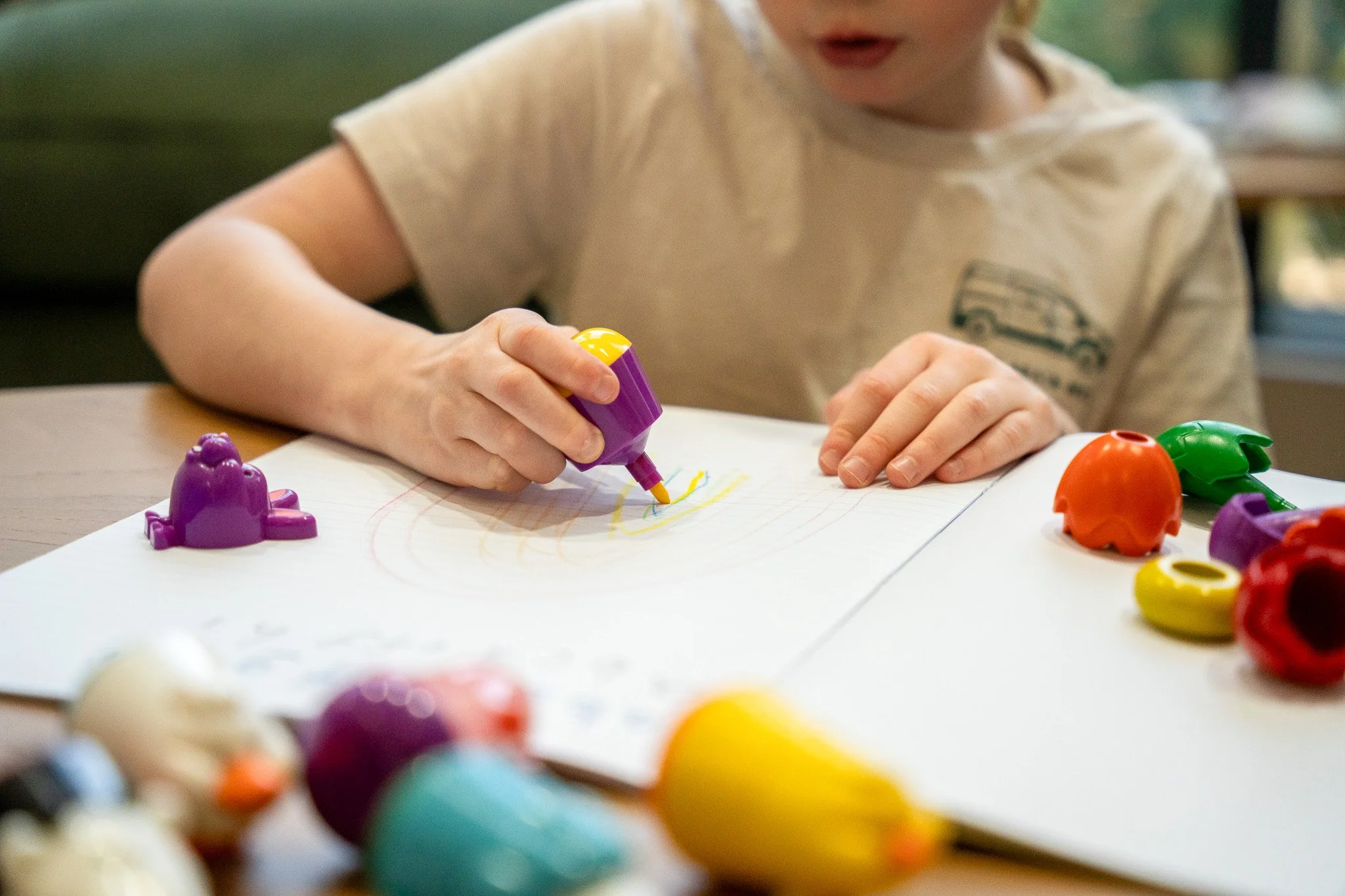 Child drawing on paper with yellow marker, surrounded by colourful animal-shaped objects - Family-friendly therapy clinic Melbourne.