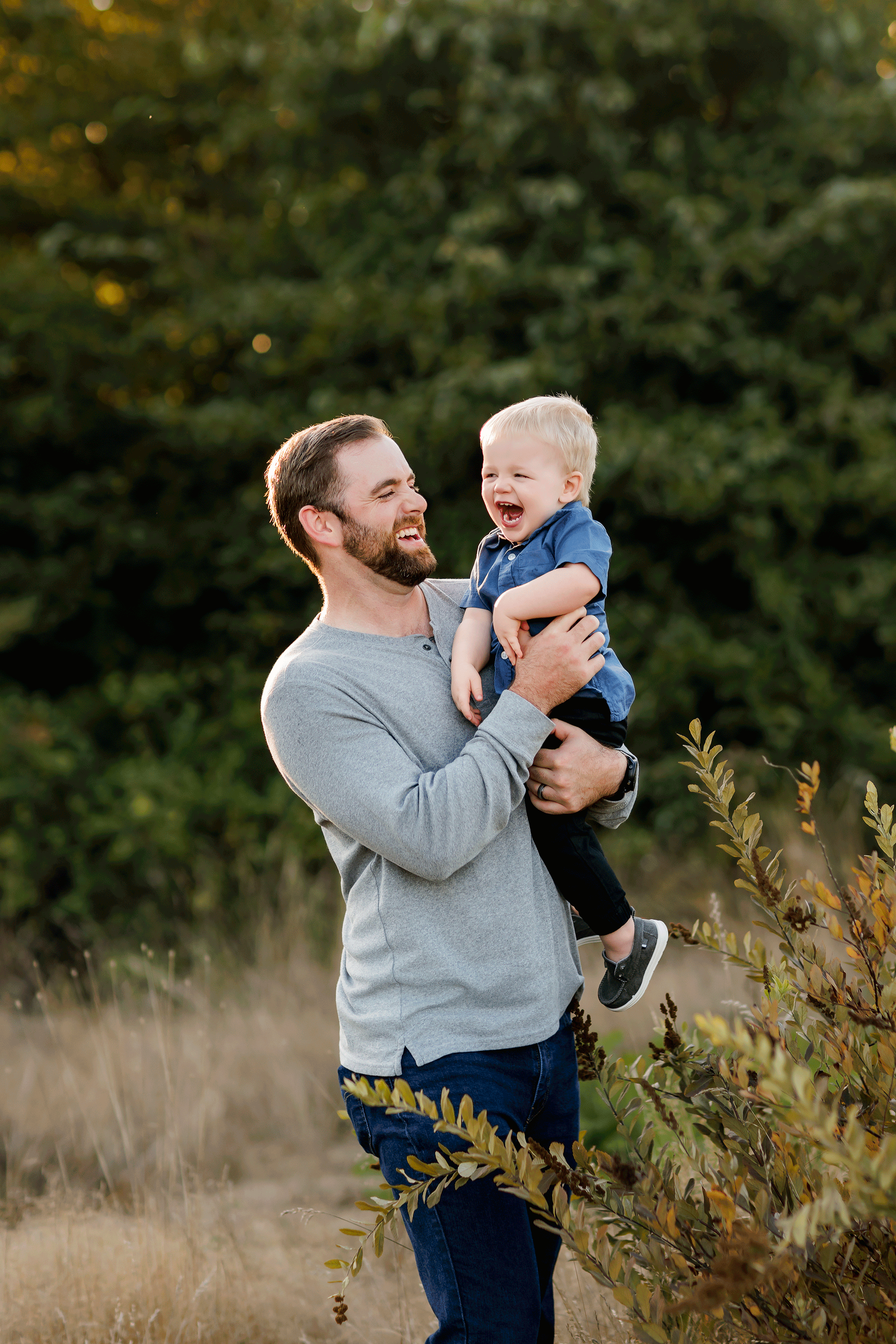 Dad holding and laughing with toddler son during outdoor family session in golden light.
