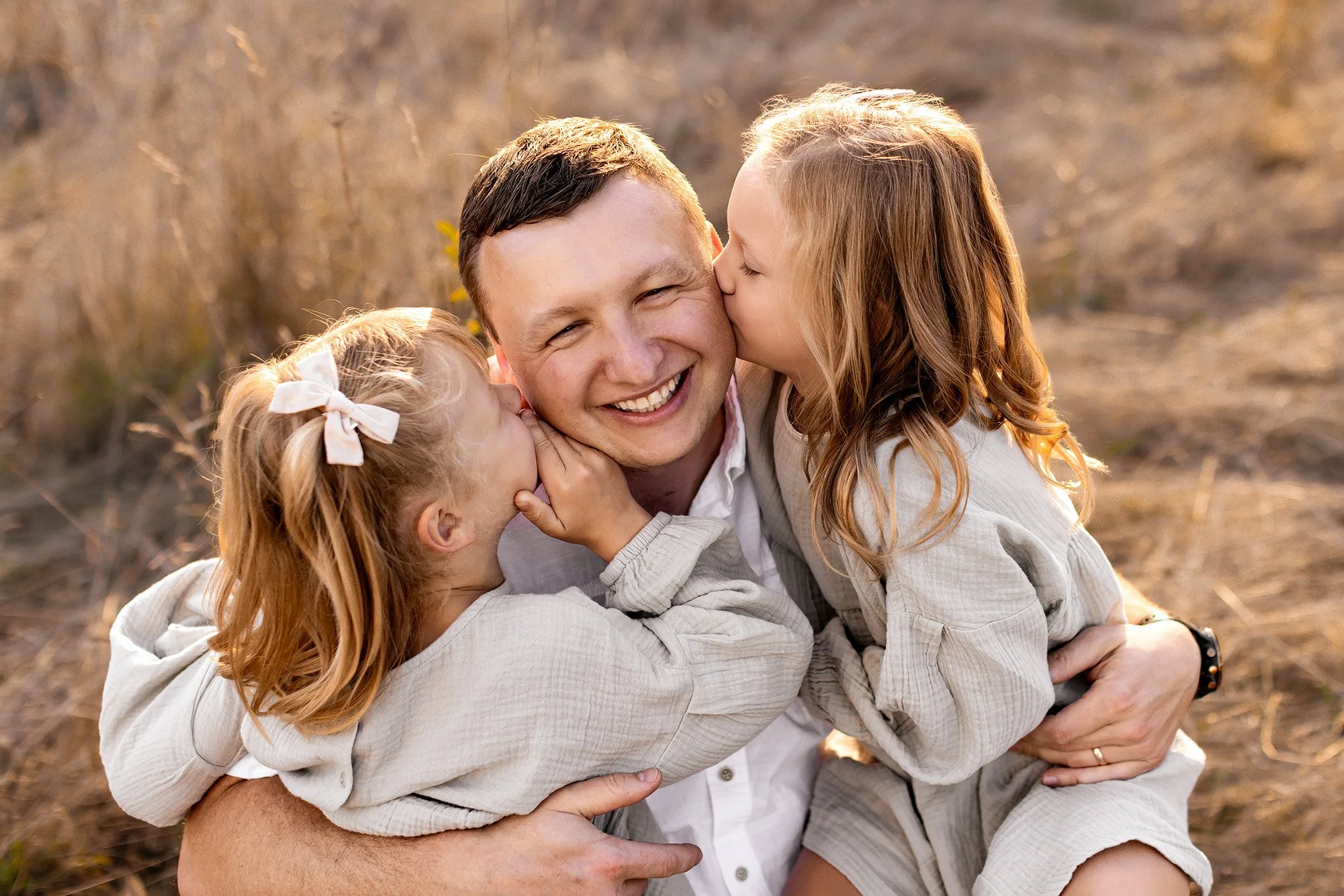 Two daughters kissing dad’s cheeks during golden hour family photography session in Salem Oregon