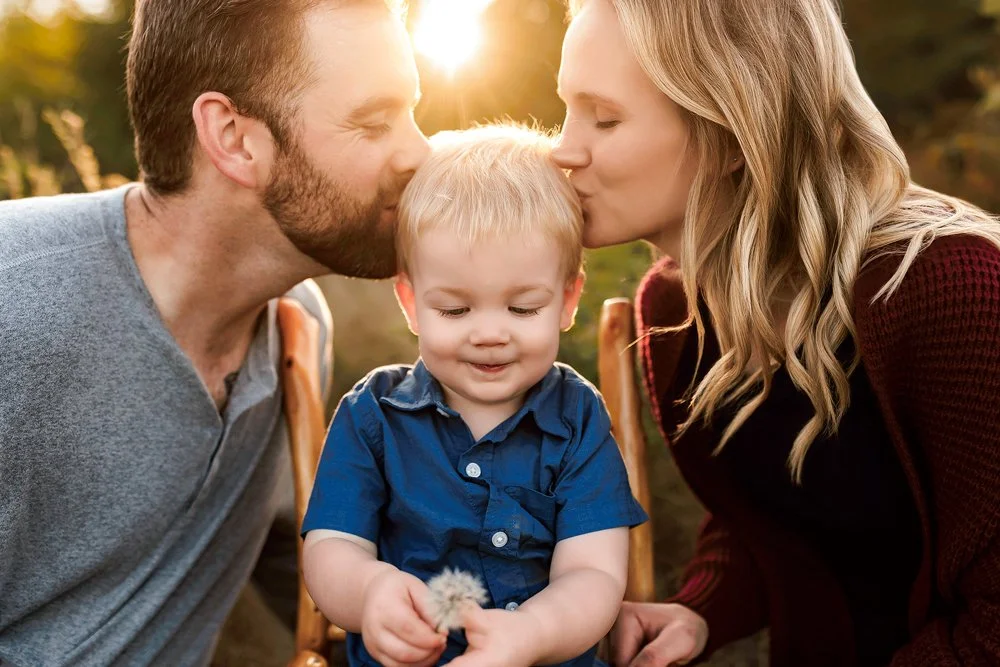 Mother and father kissing their toddler during a golden hour family photography session.