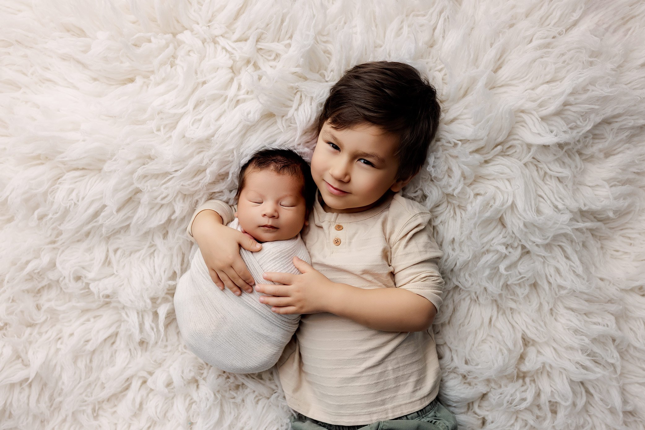 Big brother gently holding his newborn sibling during a professional newborn photography session in Salem, Oregon.