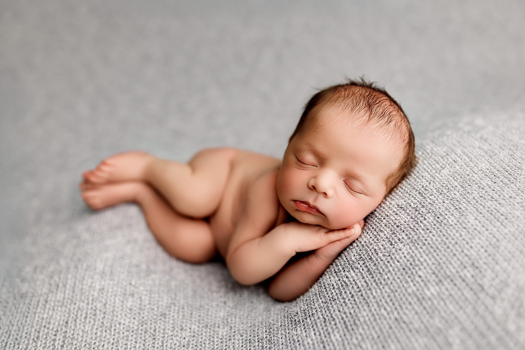 Side laying newborn photography pose on a soft textured blanket.